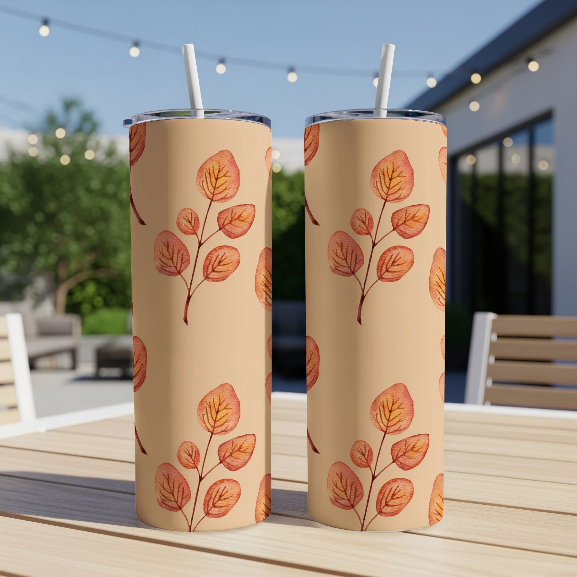 Two beige tumblers with orange and brown leaf pattern on a wooden table outdoors.