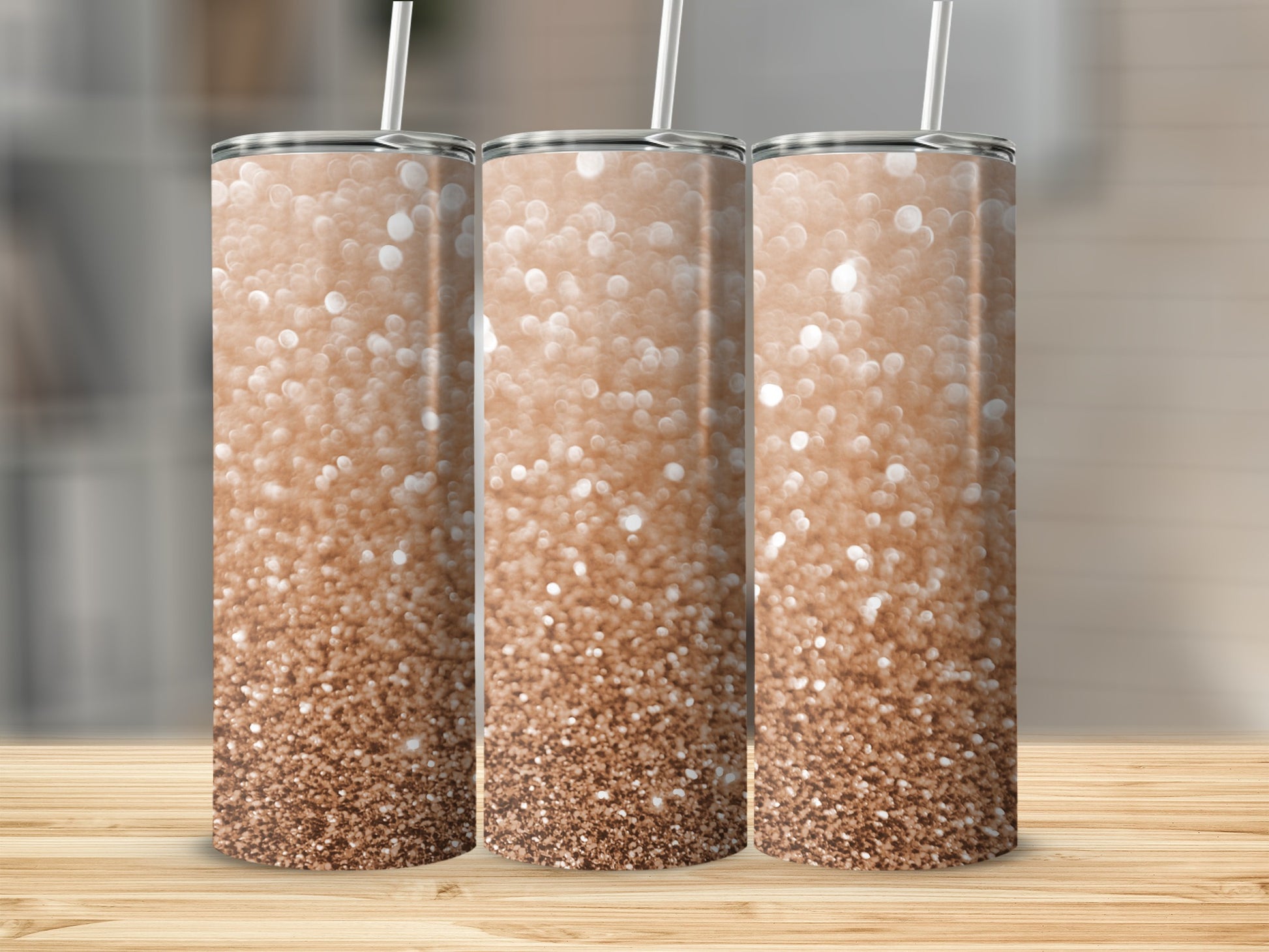 Three rose gold glitter tumblers with straws displayed on a wooden surface.