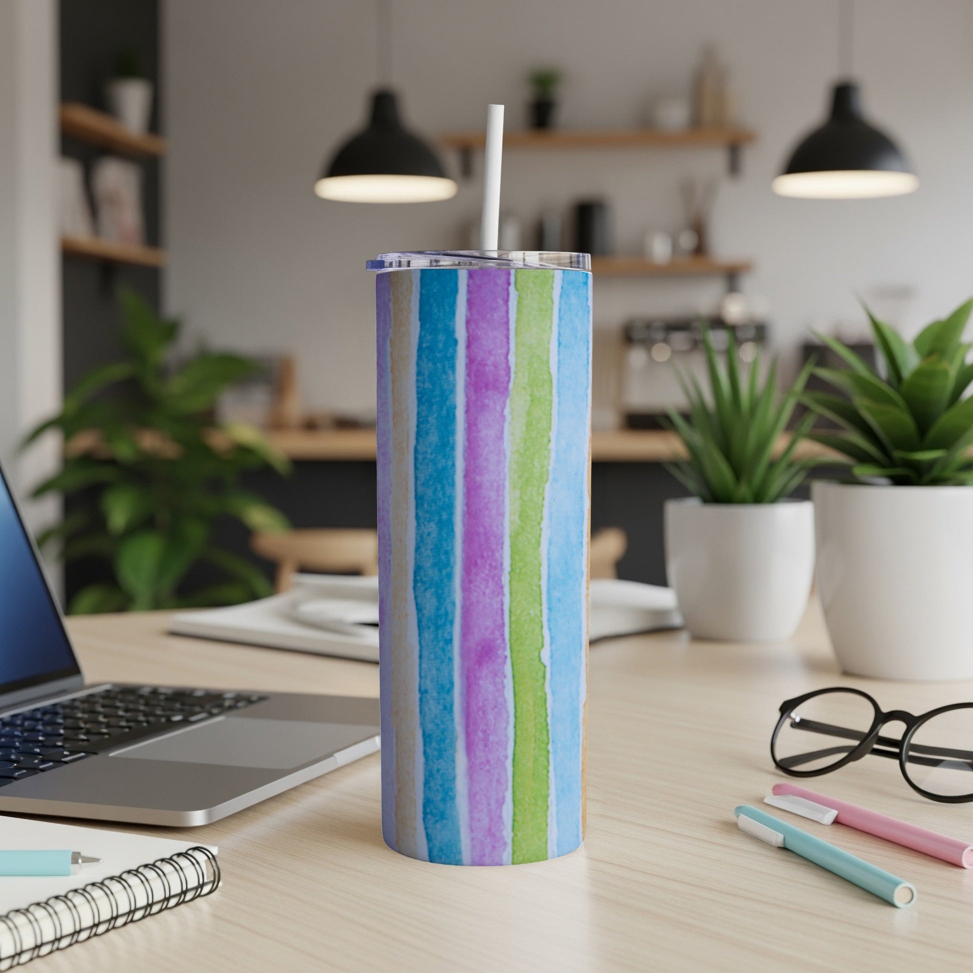 Striped blue, purple, and green tumbler with straw on a desk.