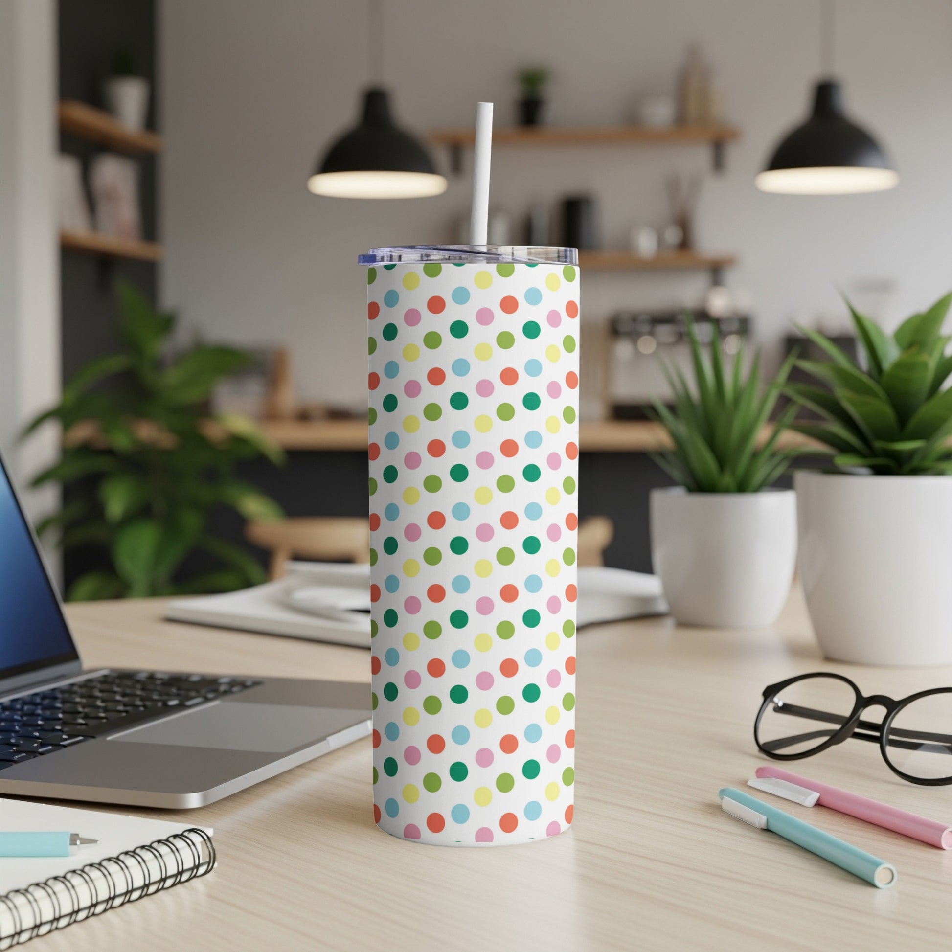 White tumbler with colorful polka dots and a straw on a desk.
