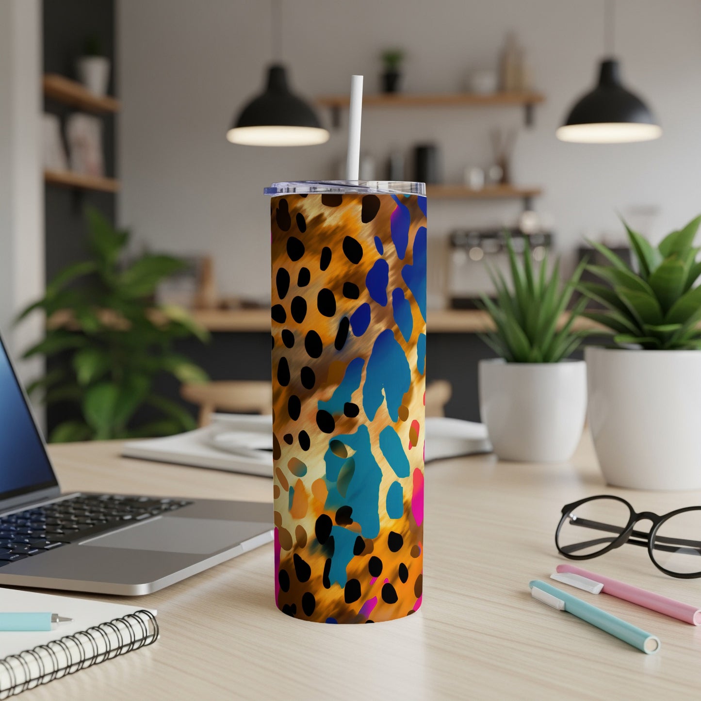 Tumbler with colorful abstract leopard spots on a desk with a laptop.