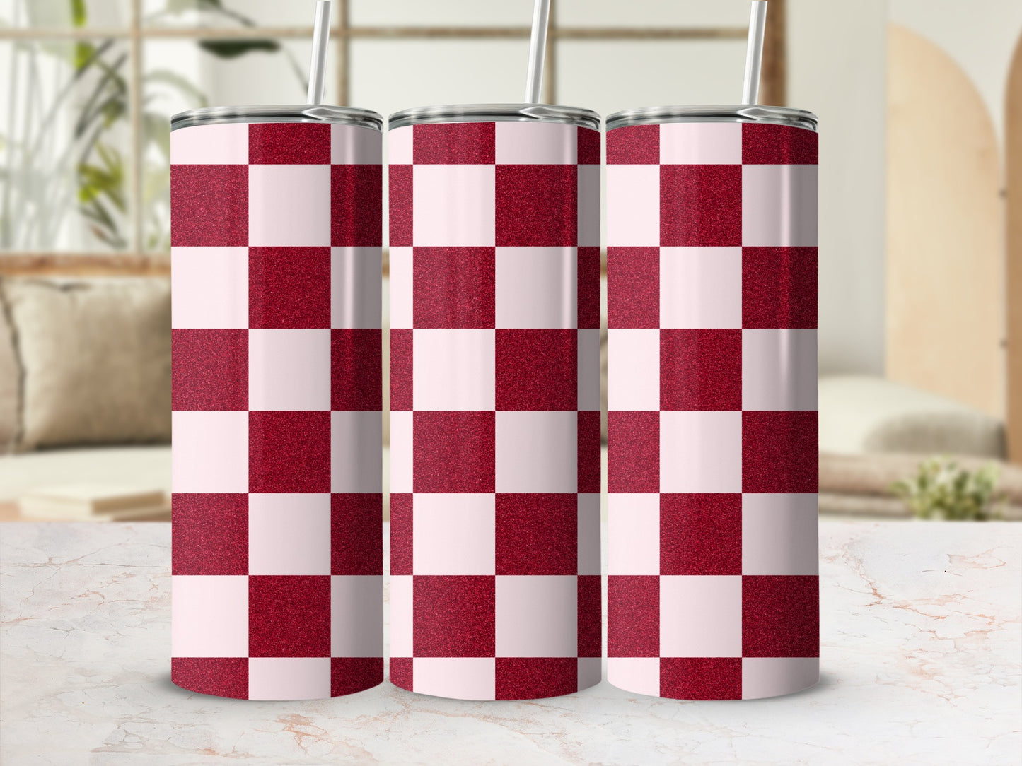 Three glittery red and white checkered tumblers with straws on a marble surface.