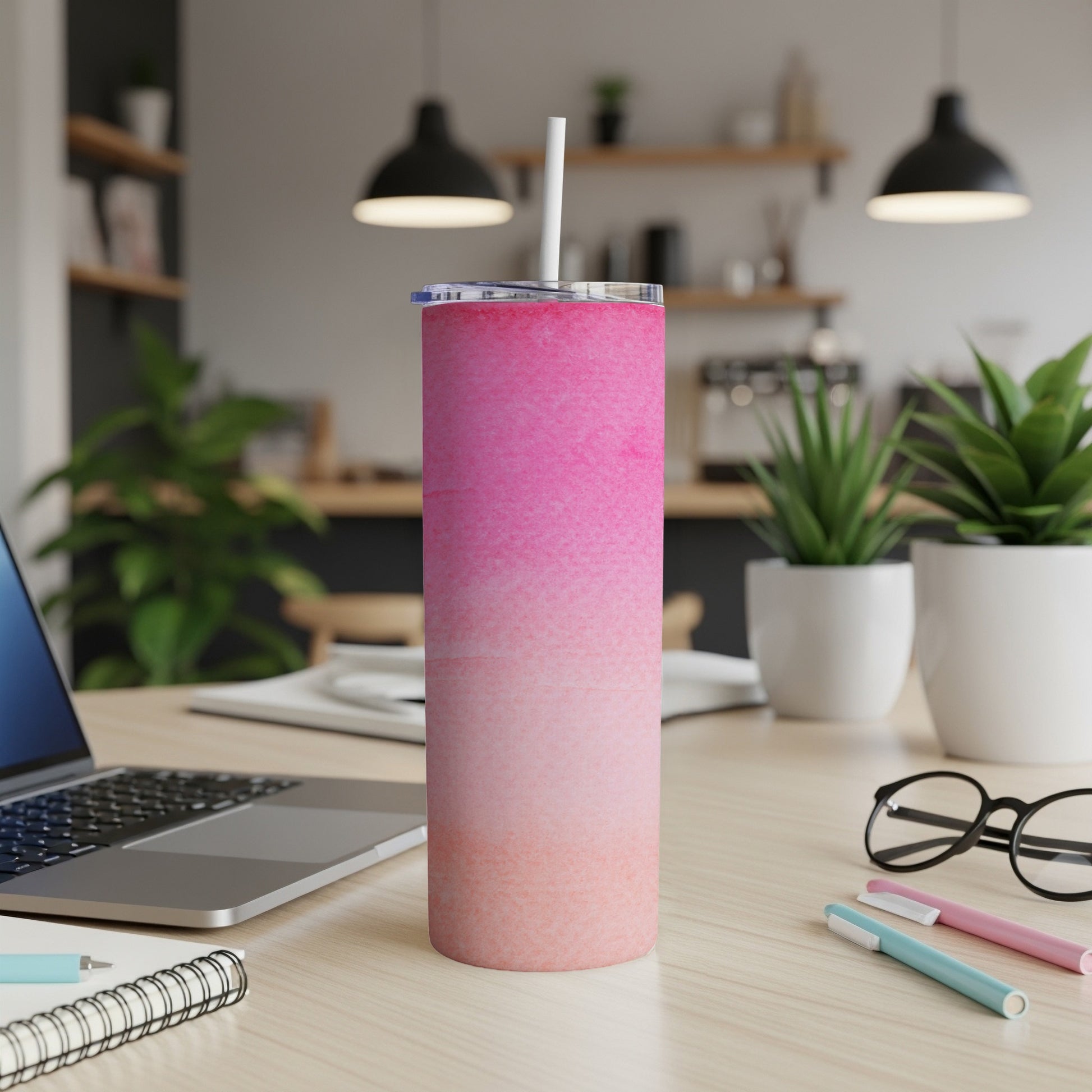 Pink gradient tumbler with straw on a desk with a laptop and pens.