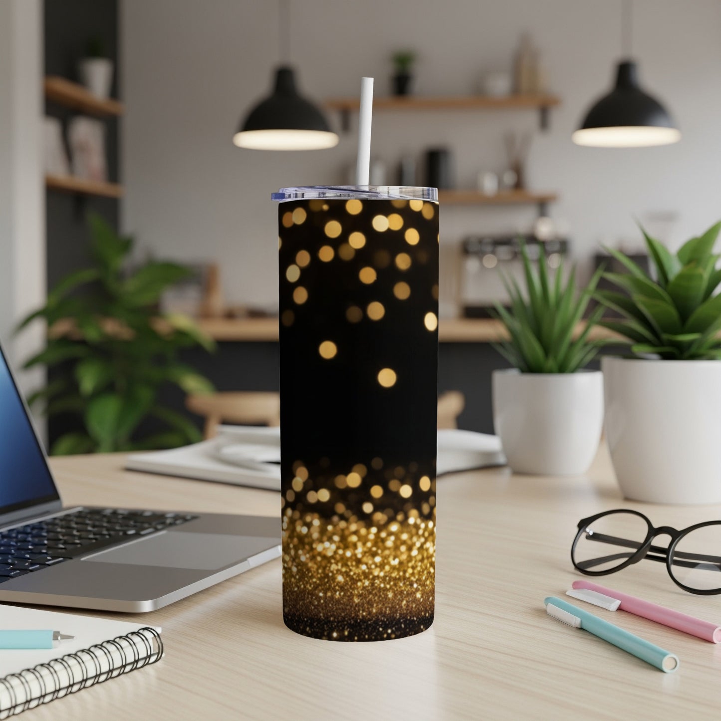 Black tumbler with sparkling gold bokeh effect and straw on desk.