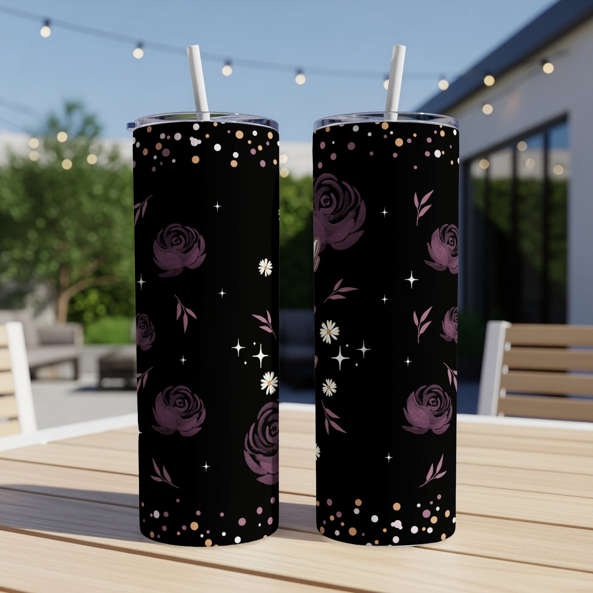Two black tumblers with purple roses and star pattern on a wooden table outdoors.
