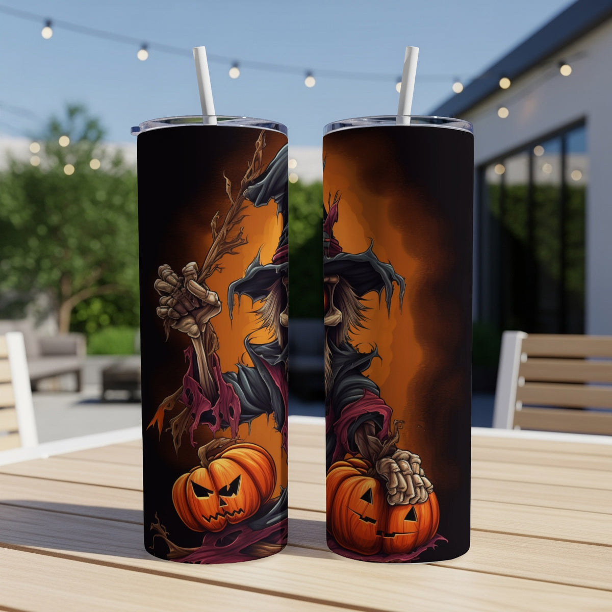 Two tumblers with Halloween scarecrow and pumpkin designs sit on a table outdoors.