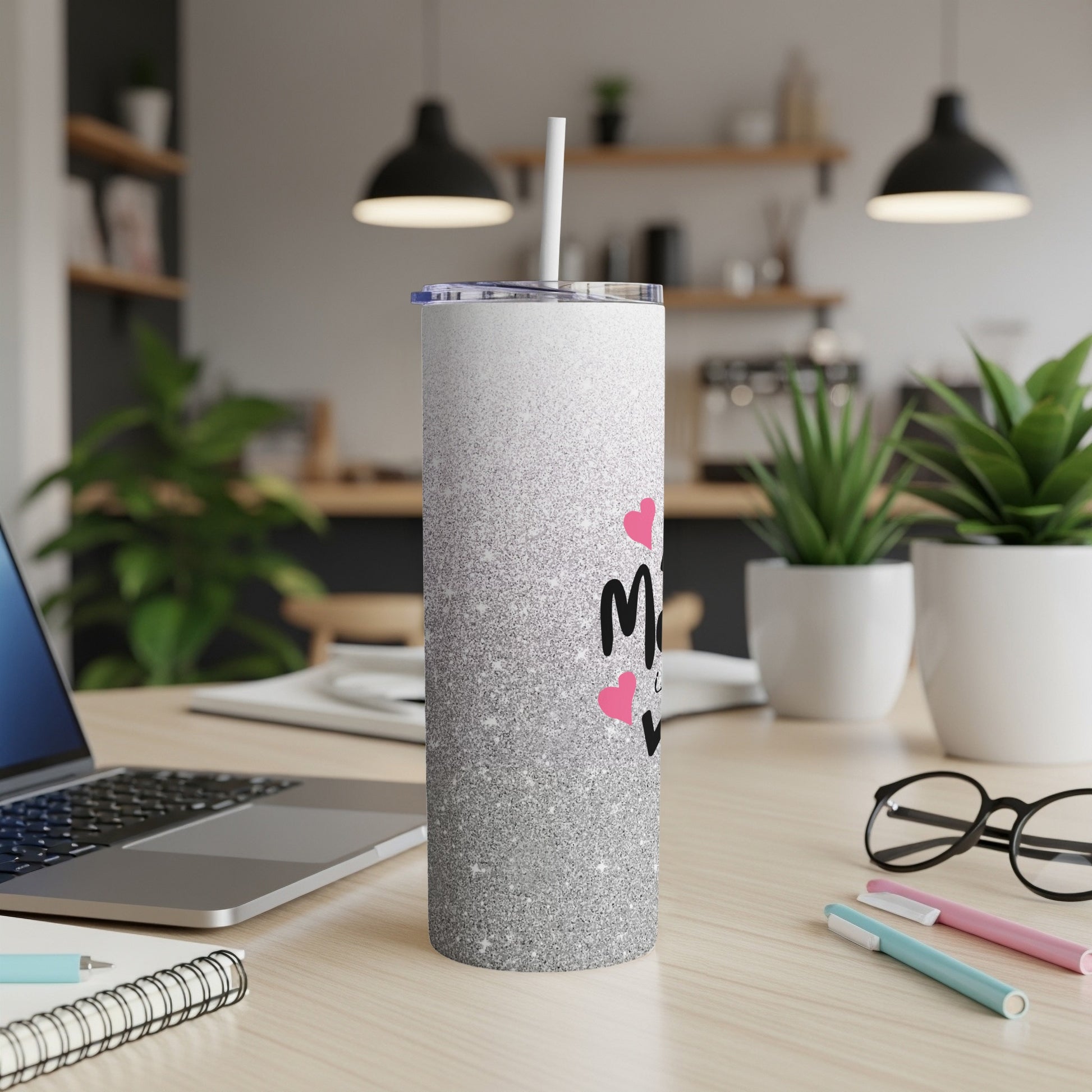 Silver glitter tumbler with "Mom" text and pink hearts, on a desk.