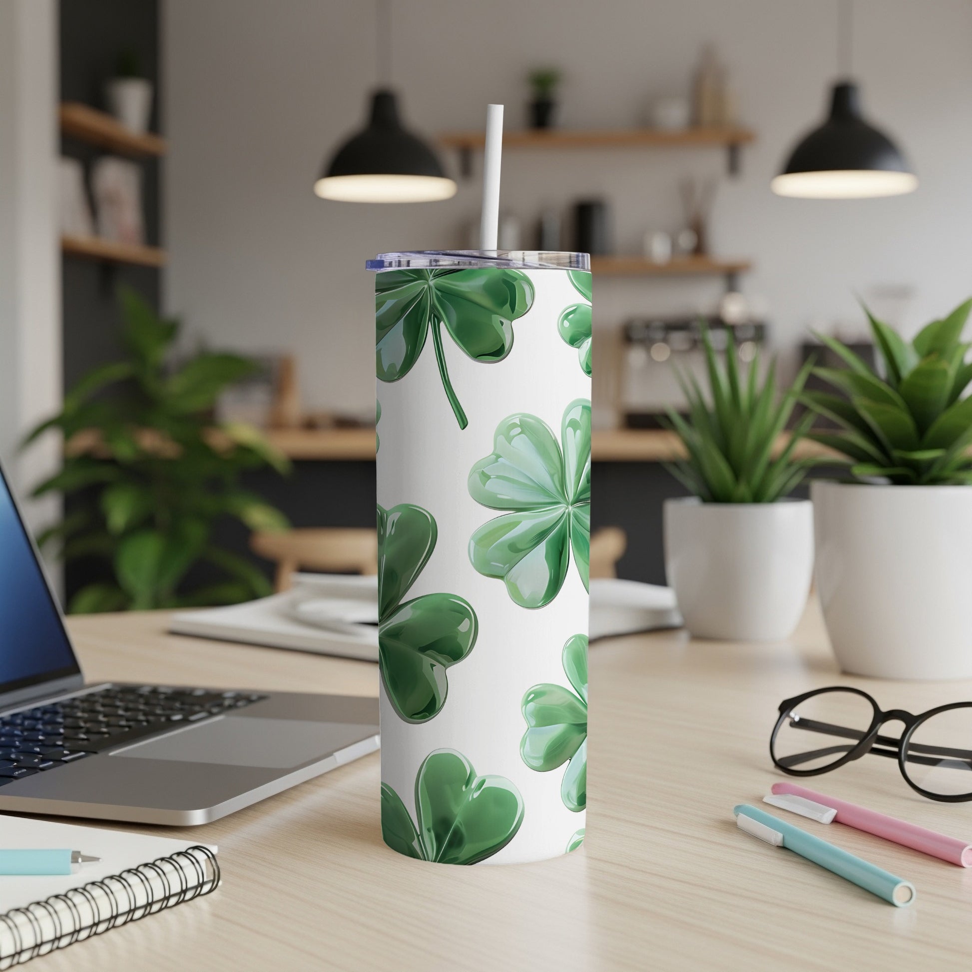 White tumbler with green shamrock pattern and straw on a desk.