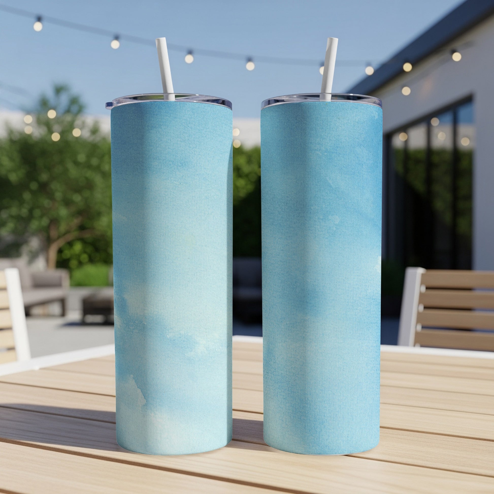 Two tall blue watercolor tumblers with straws on a wooden table.