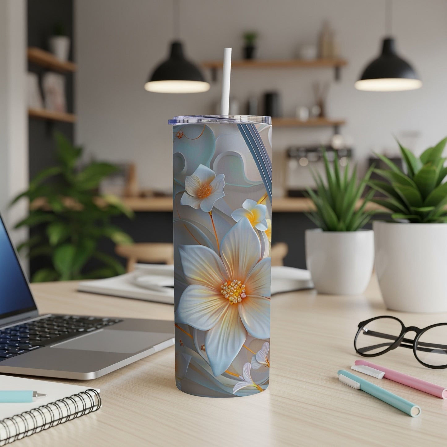 Floral design tumbler with straw on a desk with a laptop and pens.