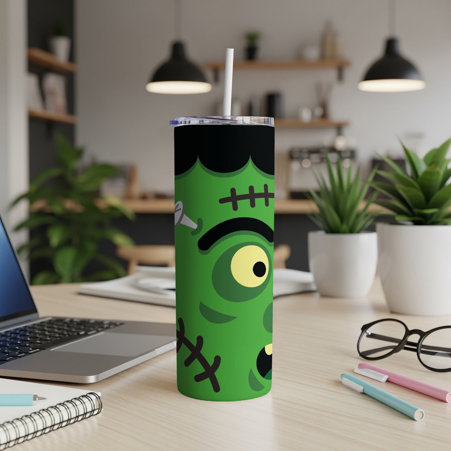 Green Frankenstein tumbler with a straw on a desk with a laptop.