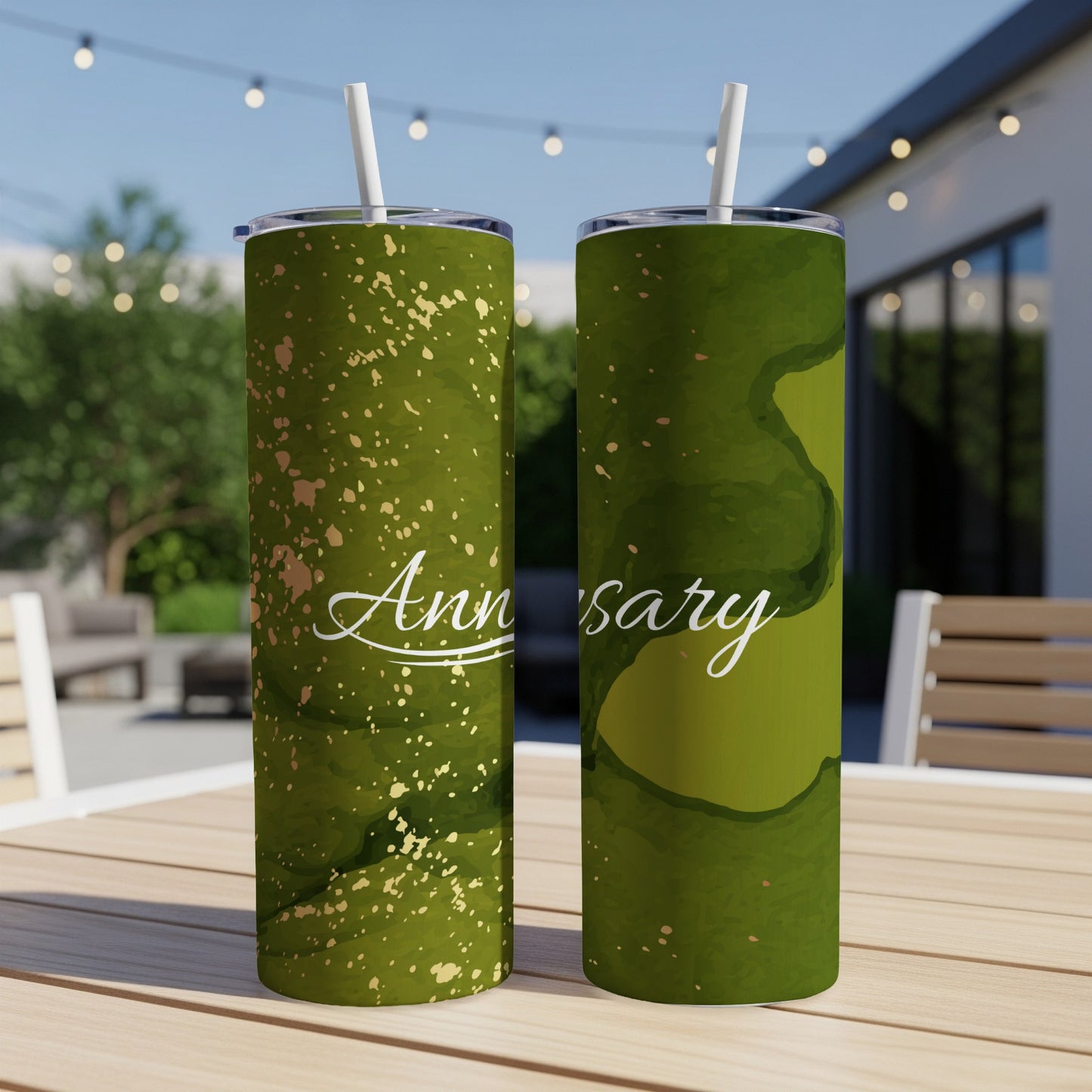 Two green tumblers with "Anniversary" text and gold splatter on an outdoor table.