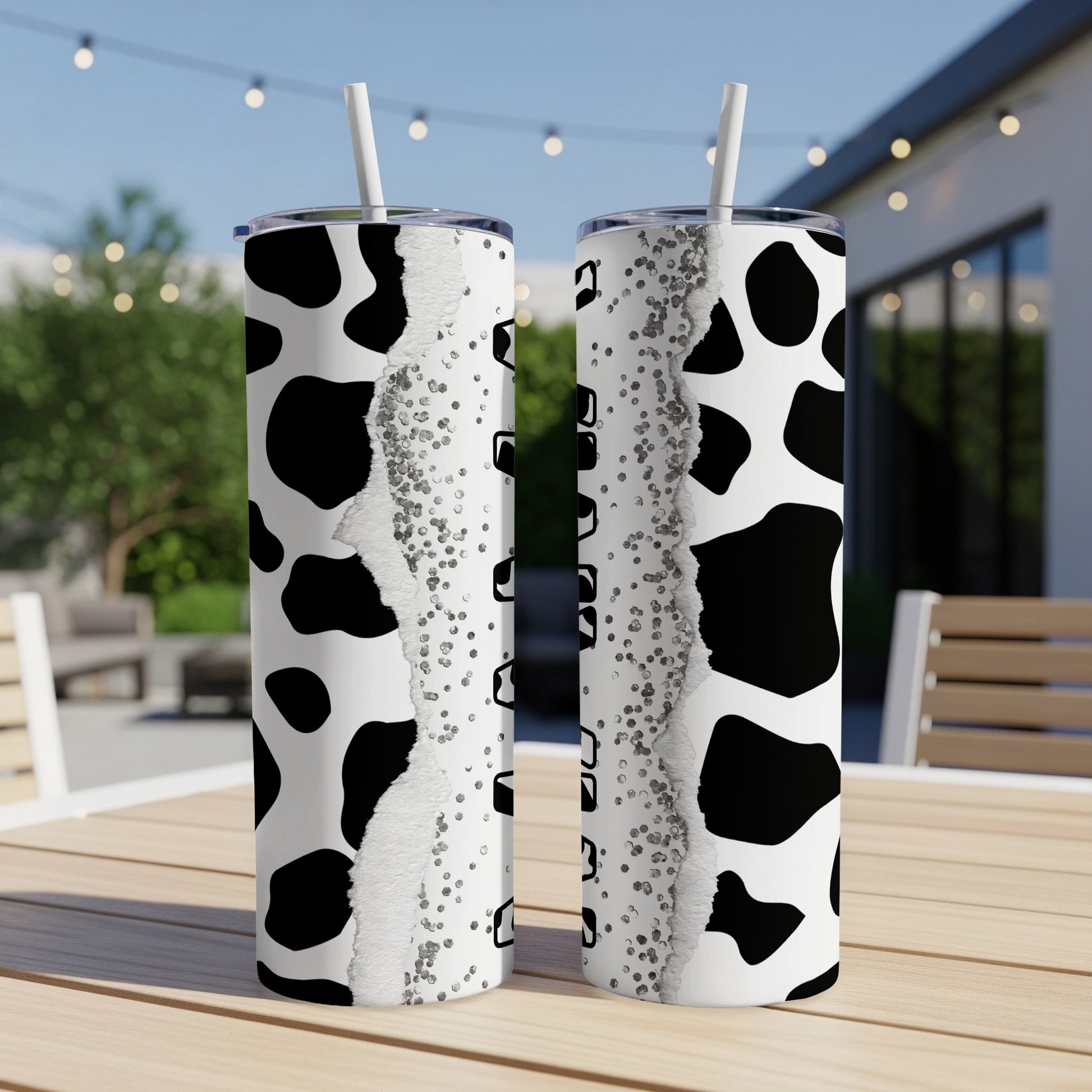 Two tumblers with cow print and glitter designs, standing on a table.