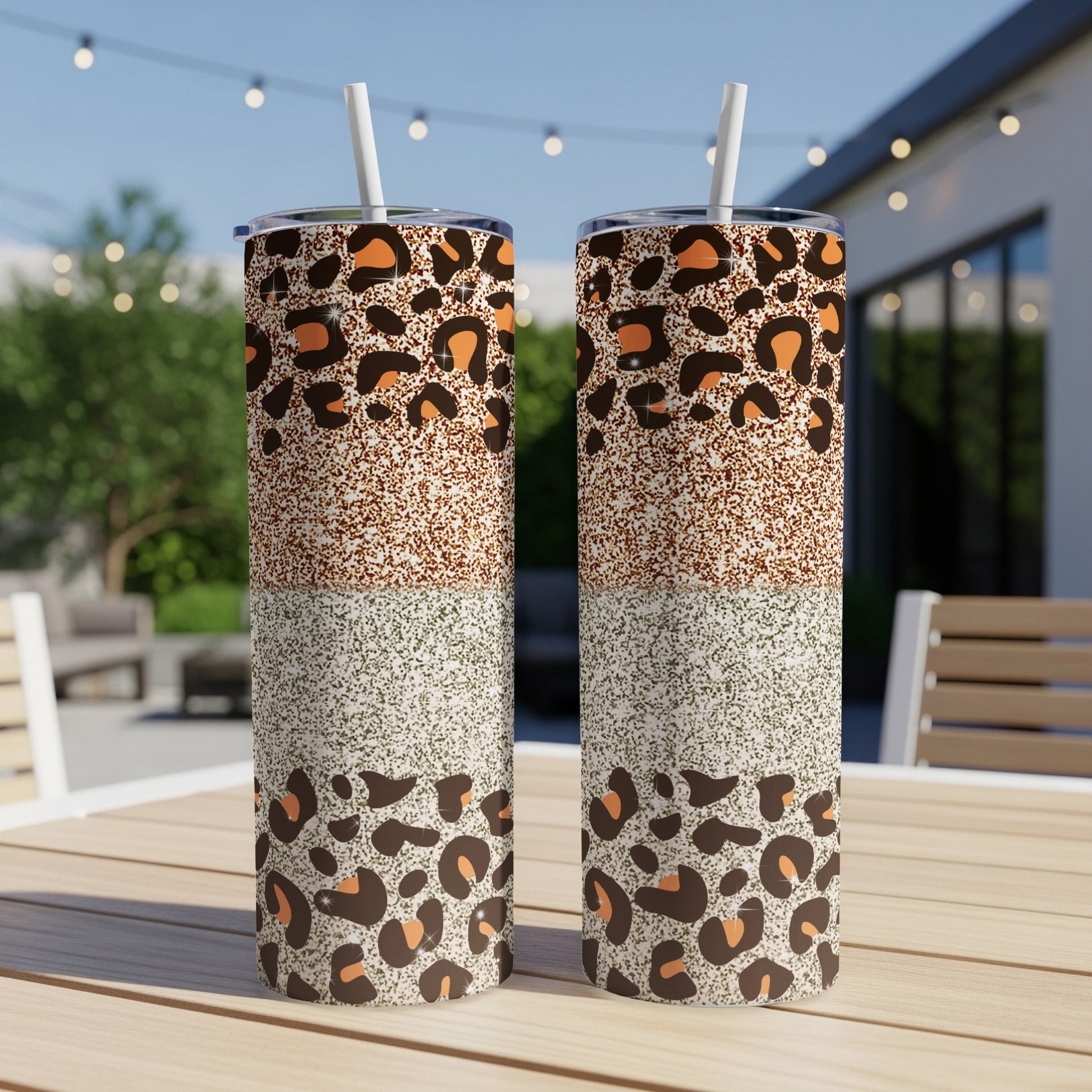 Two leopard print and glitter tumblers with straws on a table.