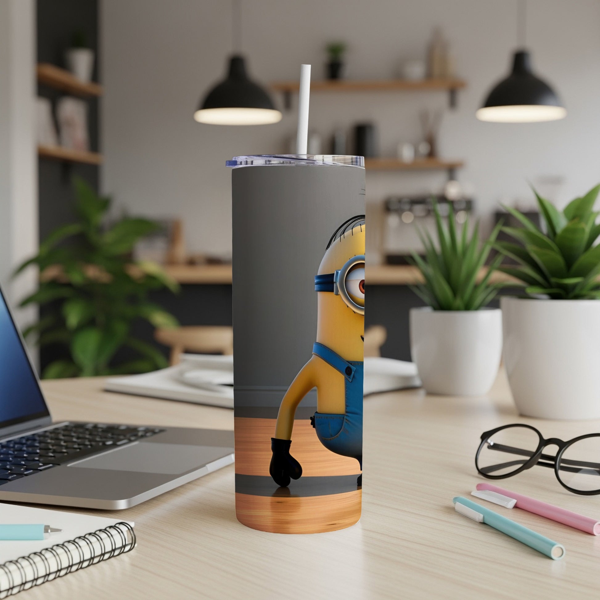 Minion character on a grey tumbler with straw, on a desk.