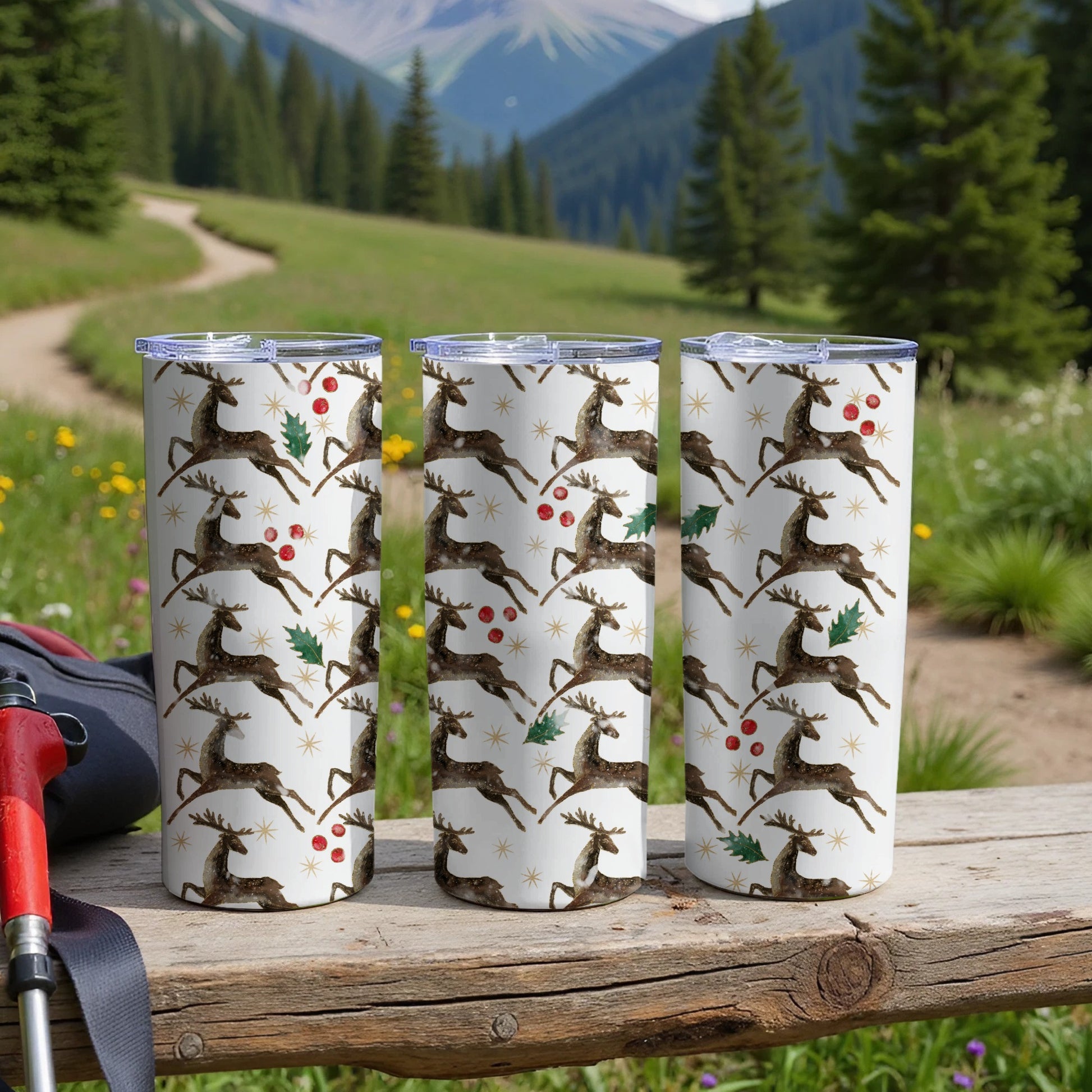Three tumblers with a deer and holly pattern on a wooden surface.