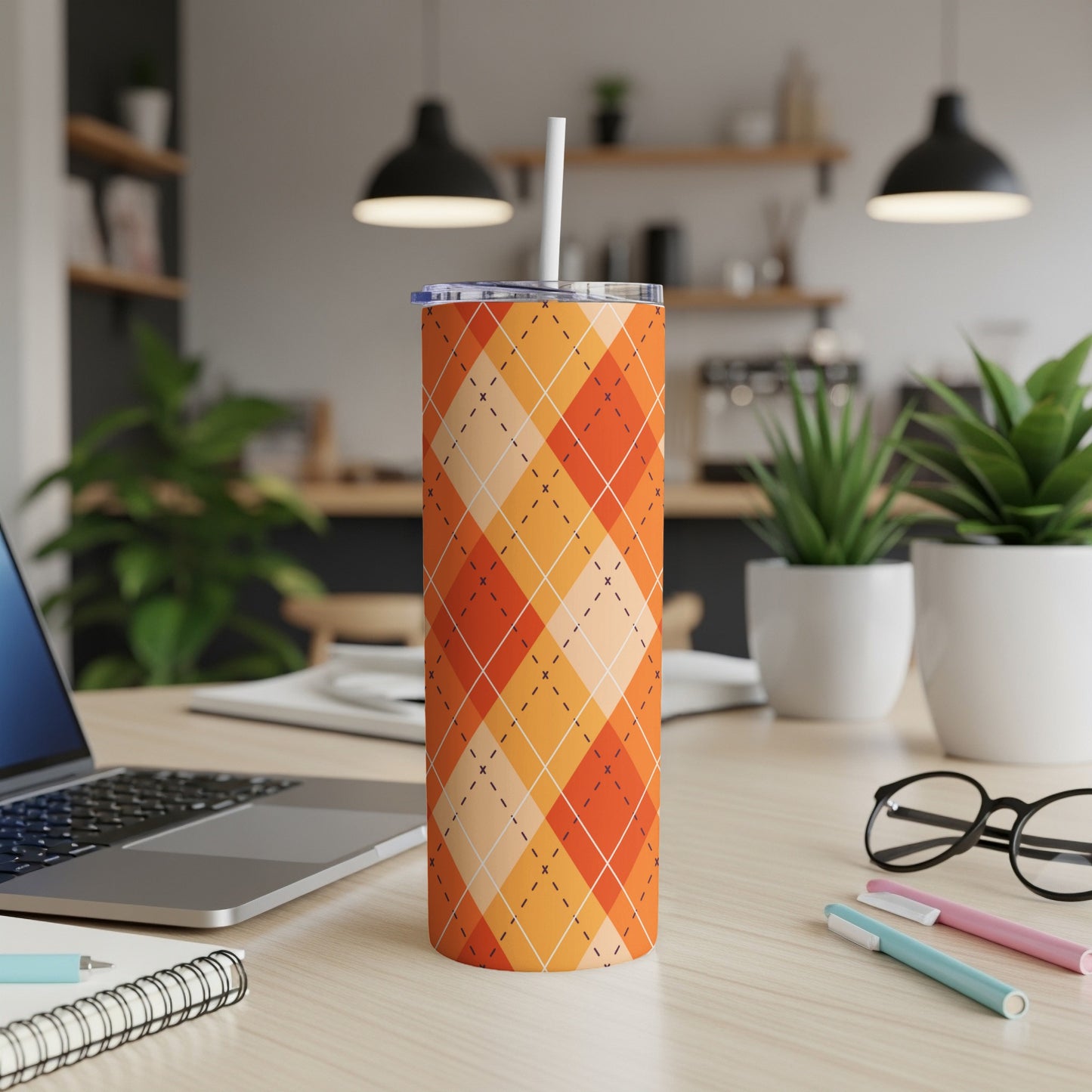 Orange argyle pattern tumbler with straw on a desk.
