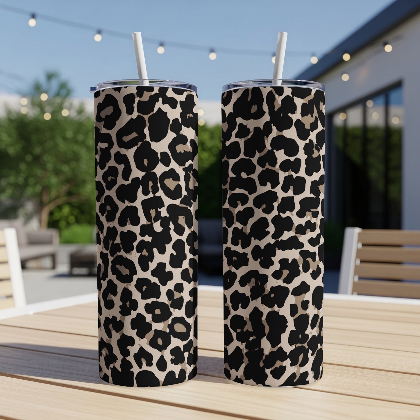 Two tan tumblers with black and beige leopard print and white straws on a wooden table.