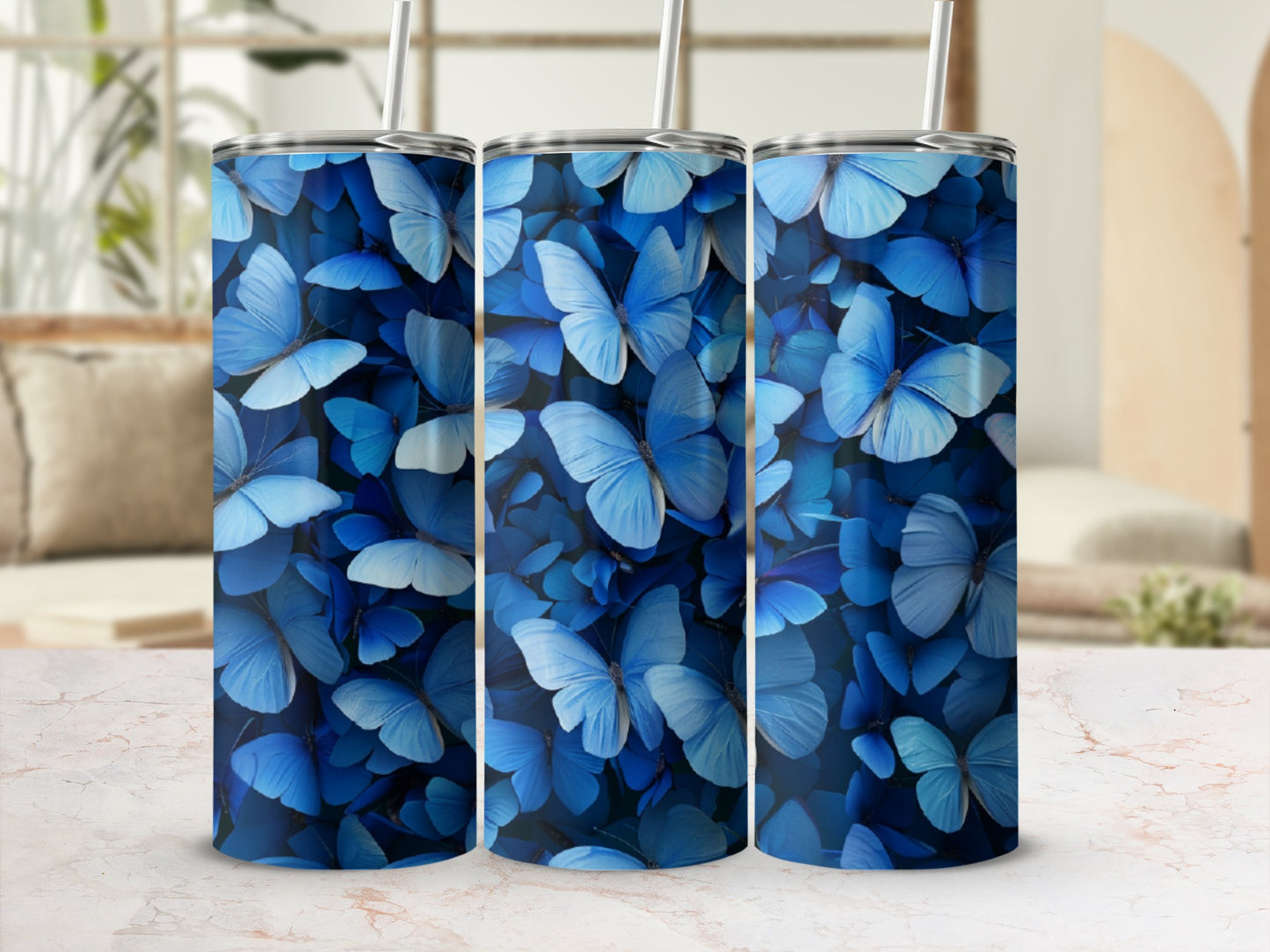 Three blue butterfly print tumblers on a marble surface with blurred background.