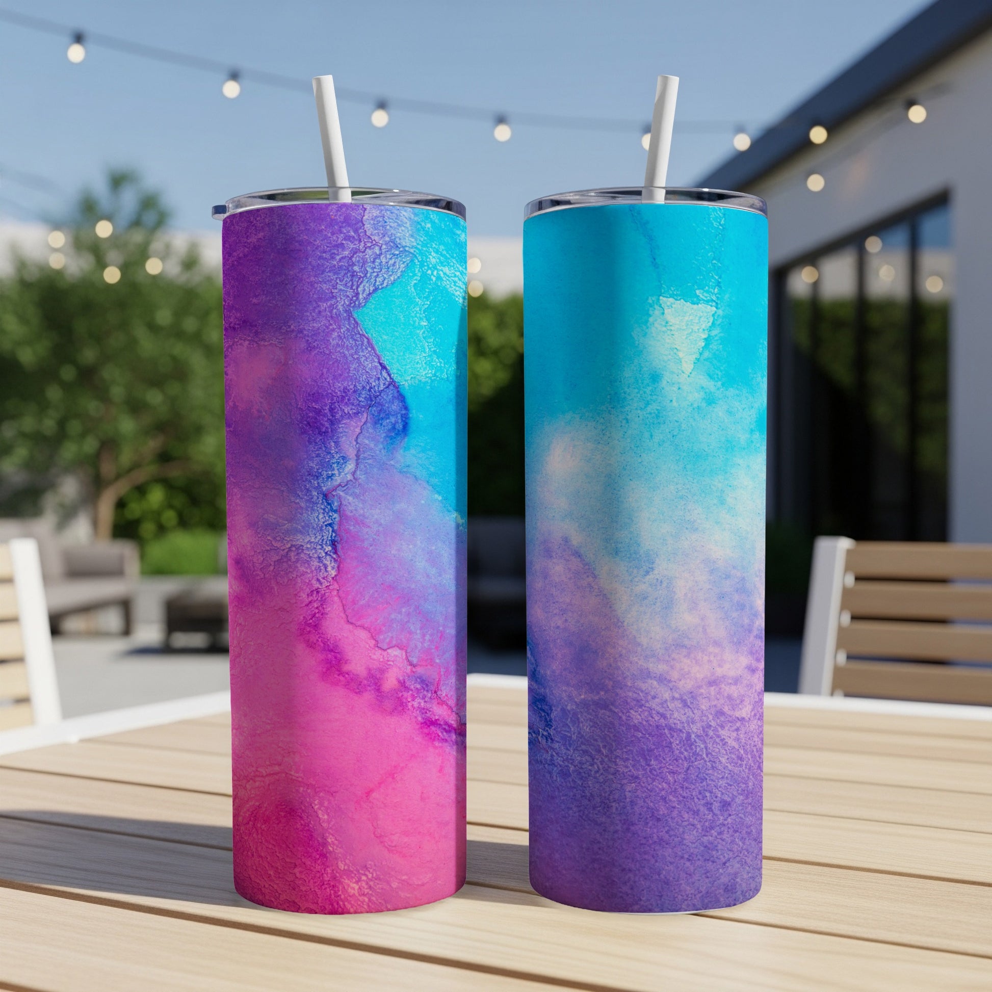 Two tumblers with pink, purple, and blue watercolor designs on a table.