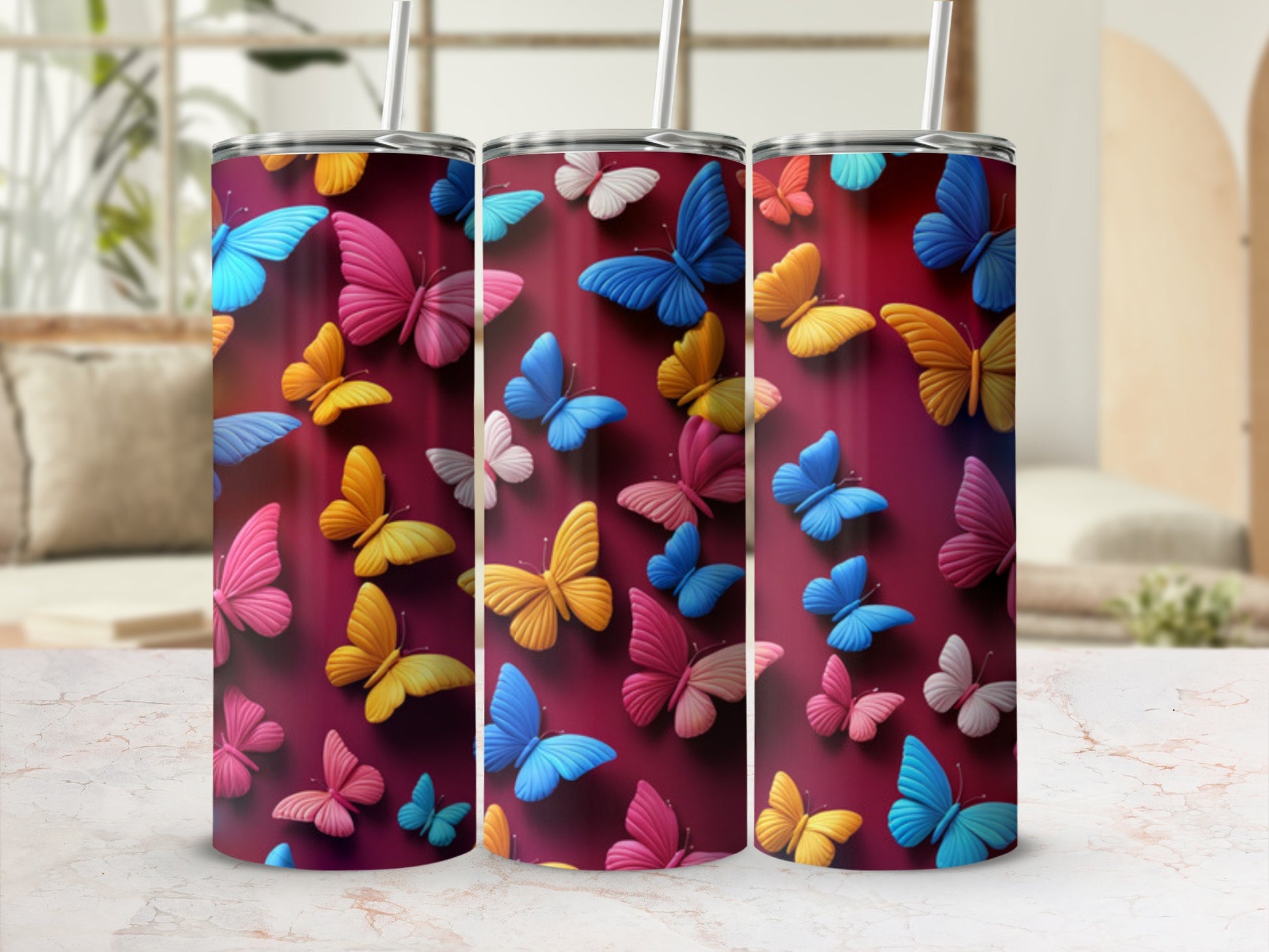 Three colorful butterfly tumblers with straws on a marble surface.
