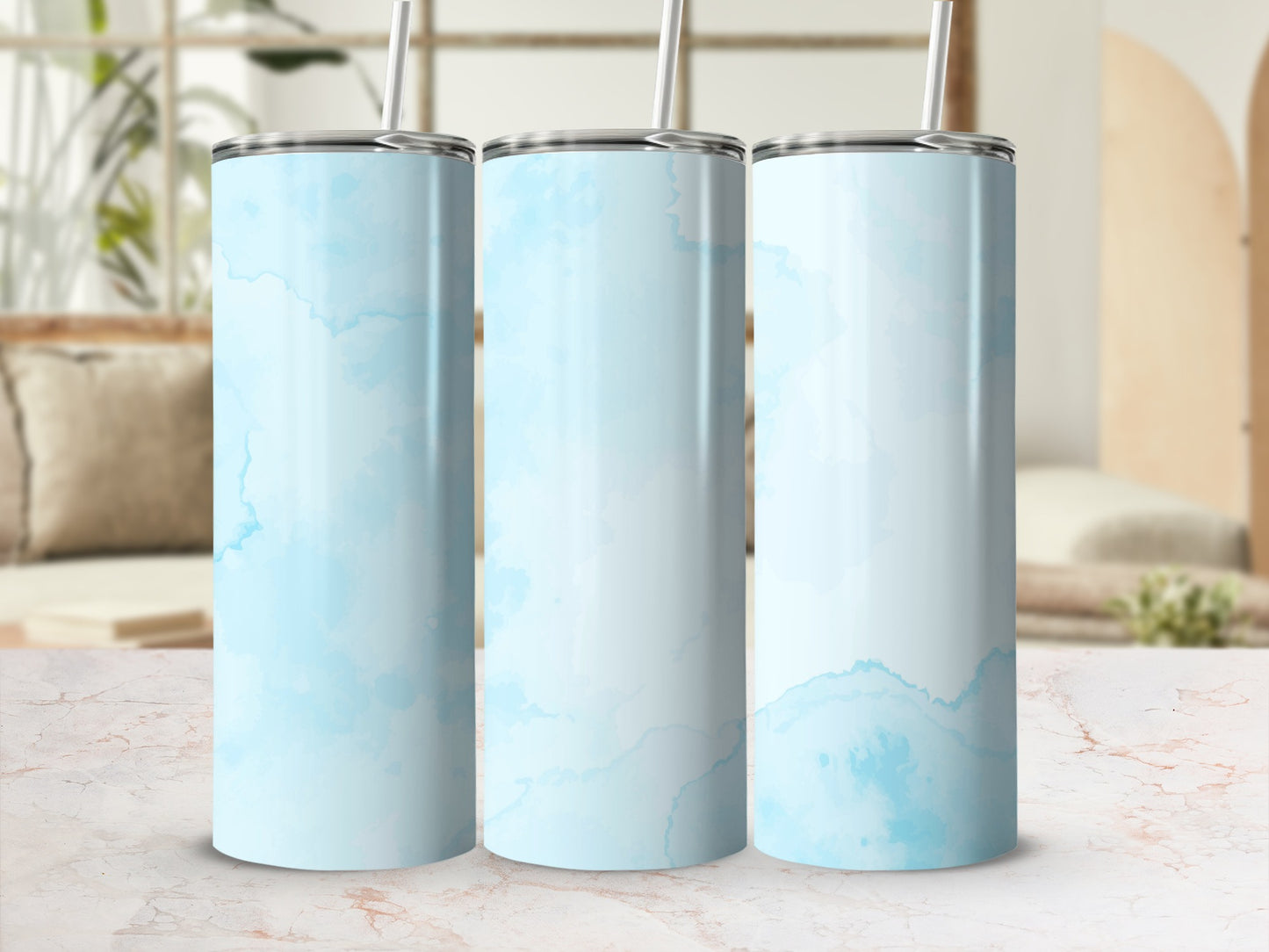 Three blue watercolor patterned tumblers with straws on a marble surface.