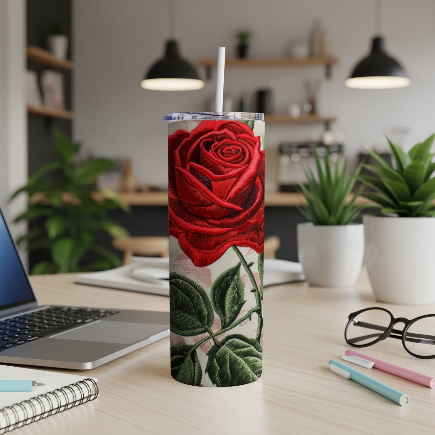 Red rose embroidered tumbler with straw on a desk.