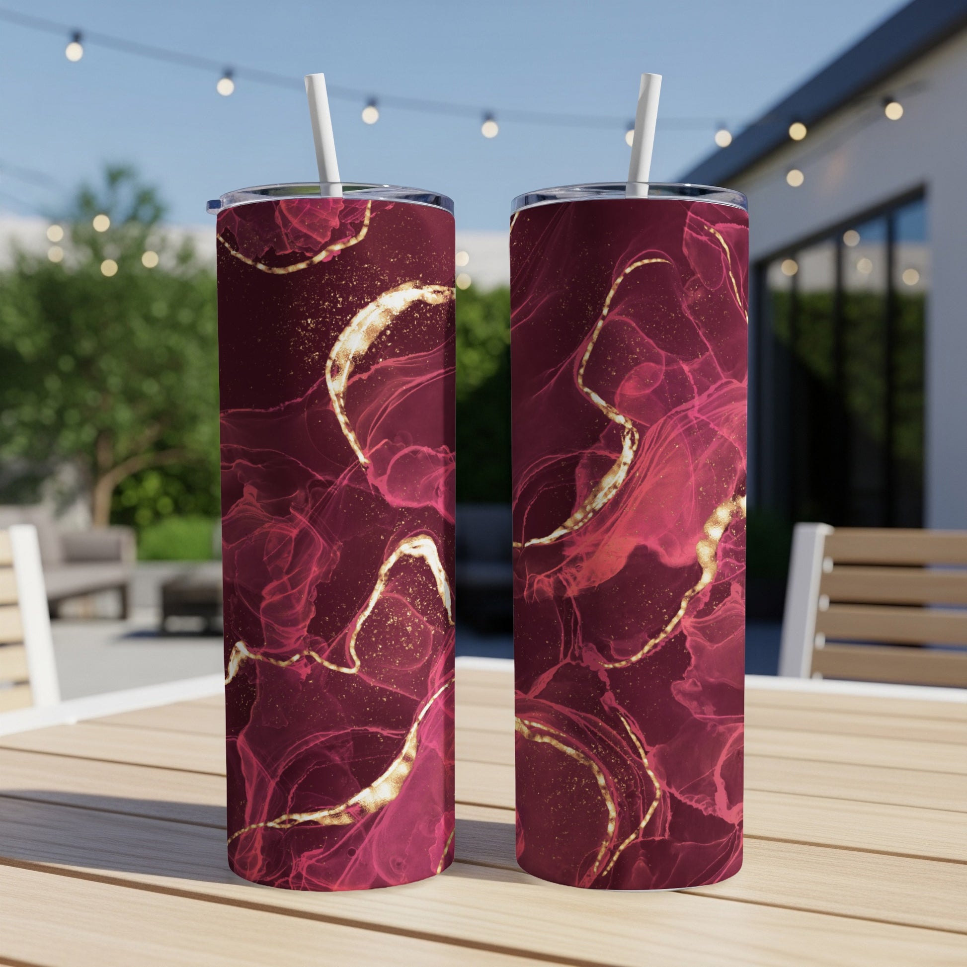 Two tumblers with swirling red and gold abstract patterns on an outdoor table.