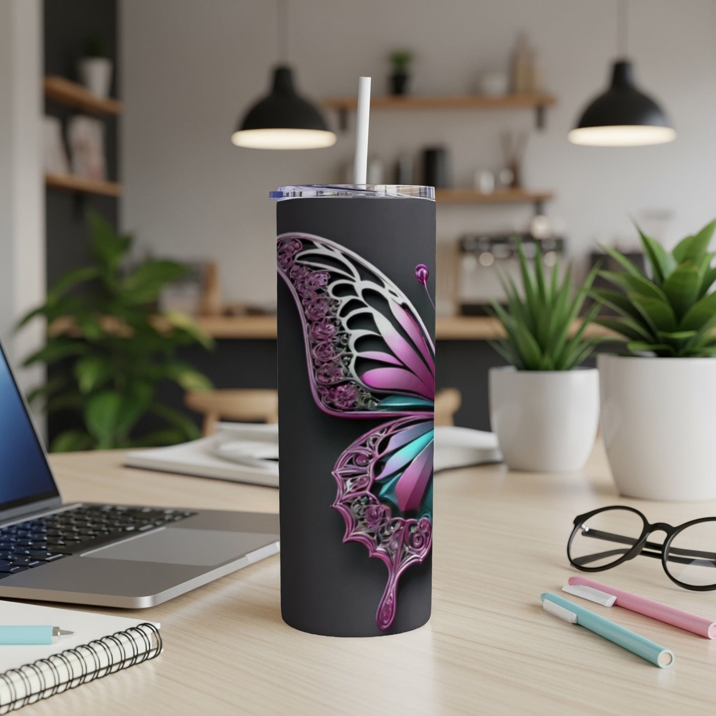 Black tumbler with a metallic butterfly design, straw, and laptop on desk.