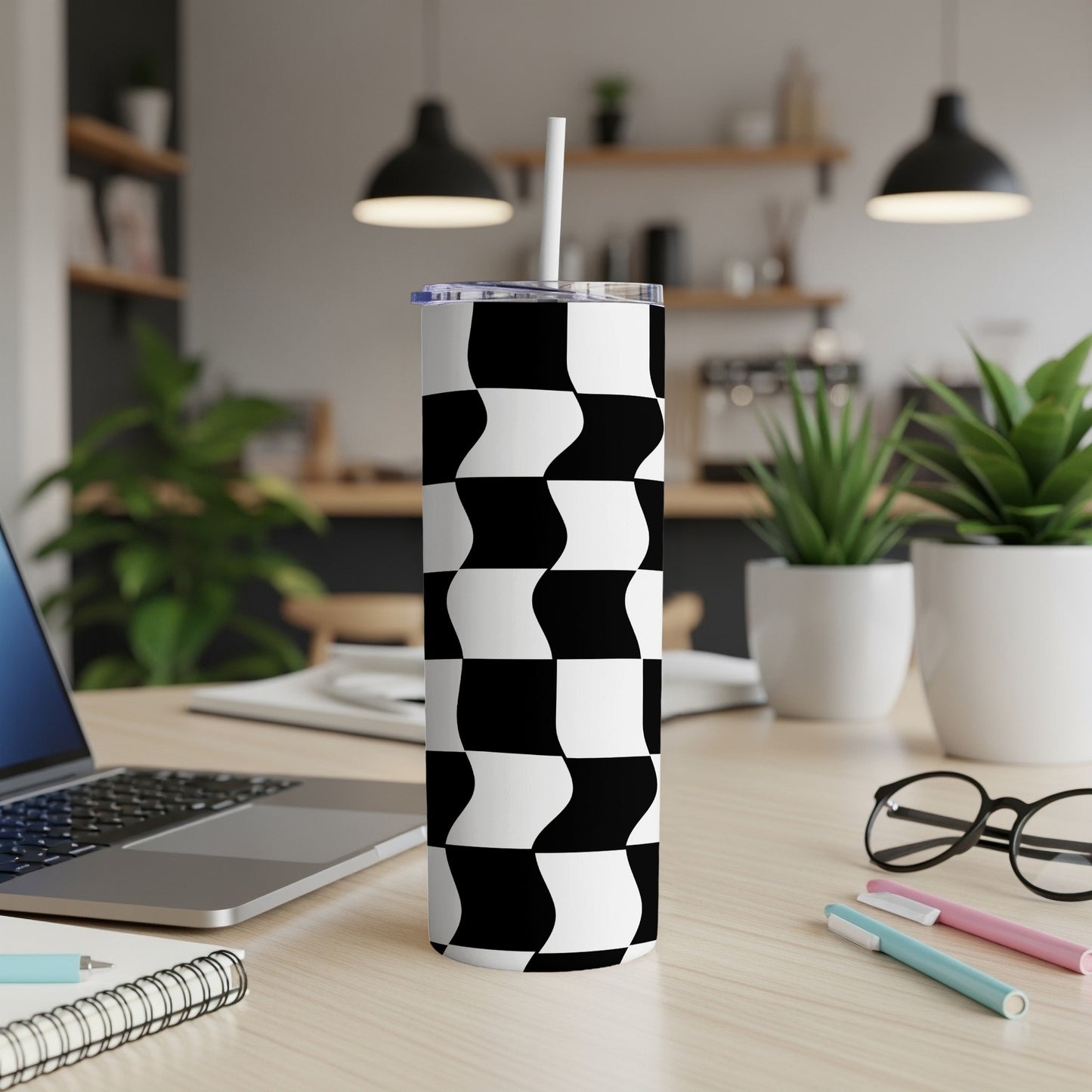 Black and white wavy checkered tumbler with straw on a desk.