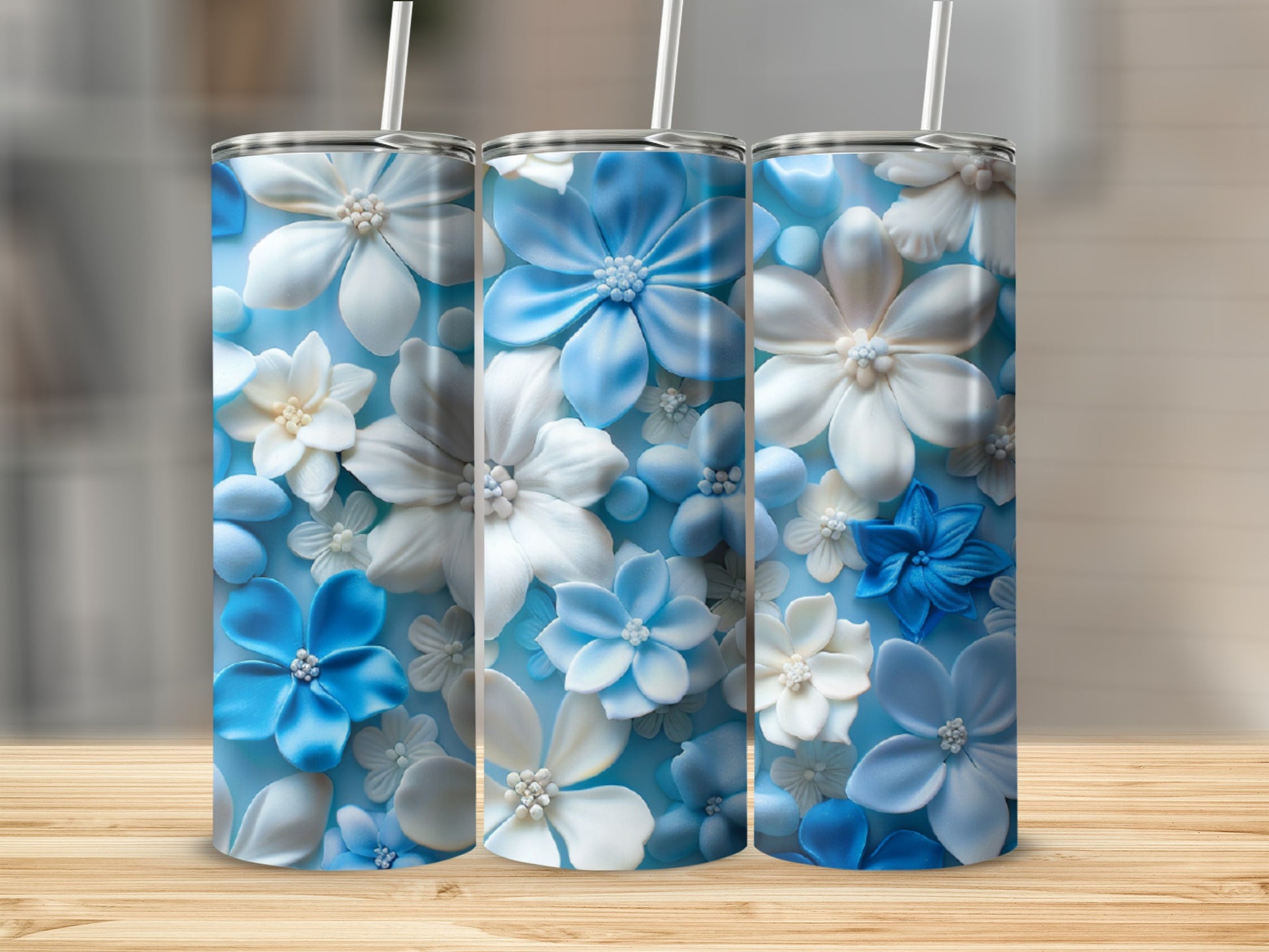 Three blue and white floral tumblers with straws on a wooden surface.