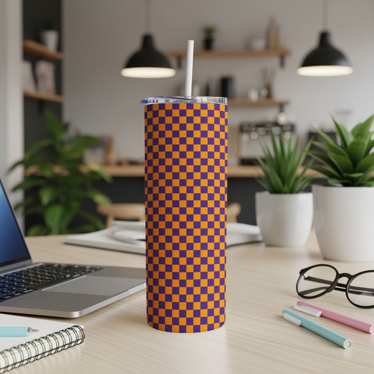 Orange and purple checkered tumbler with straw on a desk.