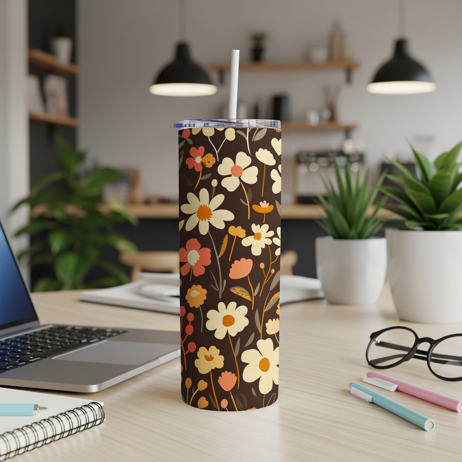 Floral tumbler with straw on a desk, next to a laptop and pens.