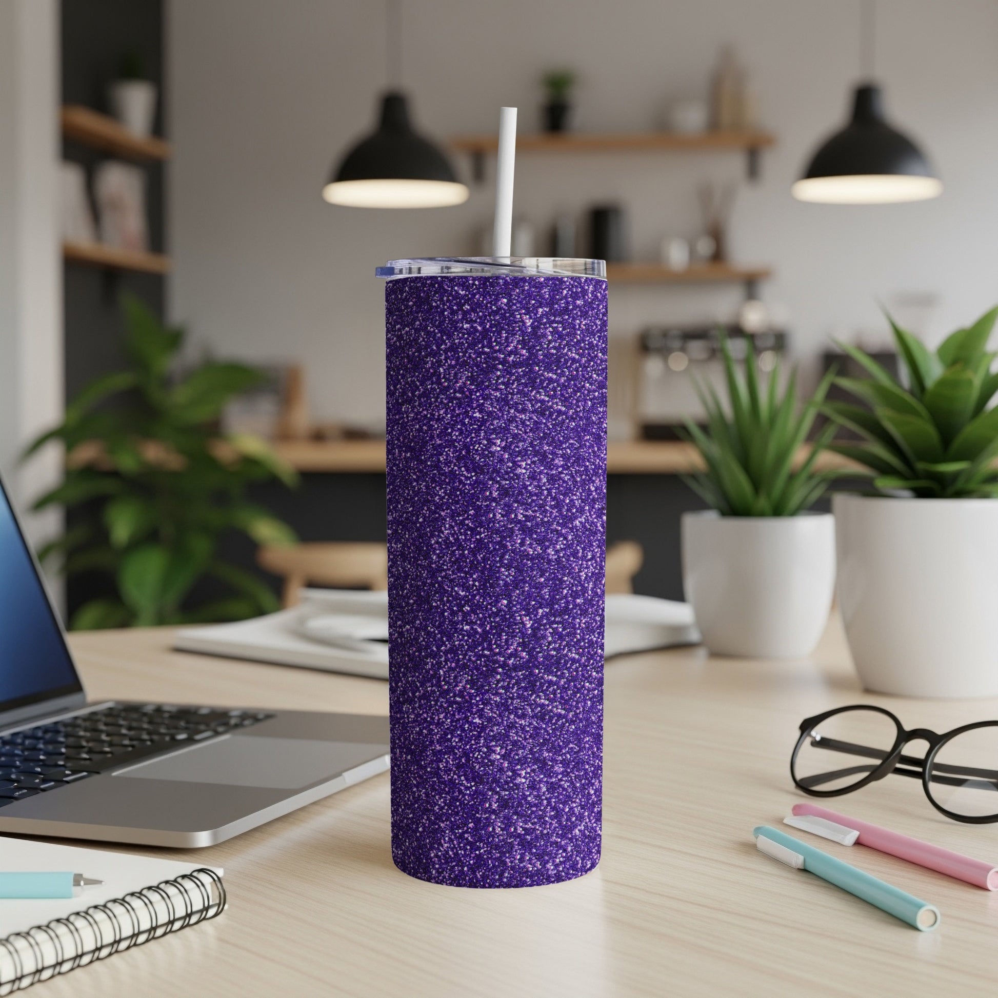 Purple glitter tumbler with straw on a desk, next to a laptop and glasses.