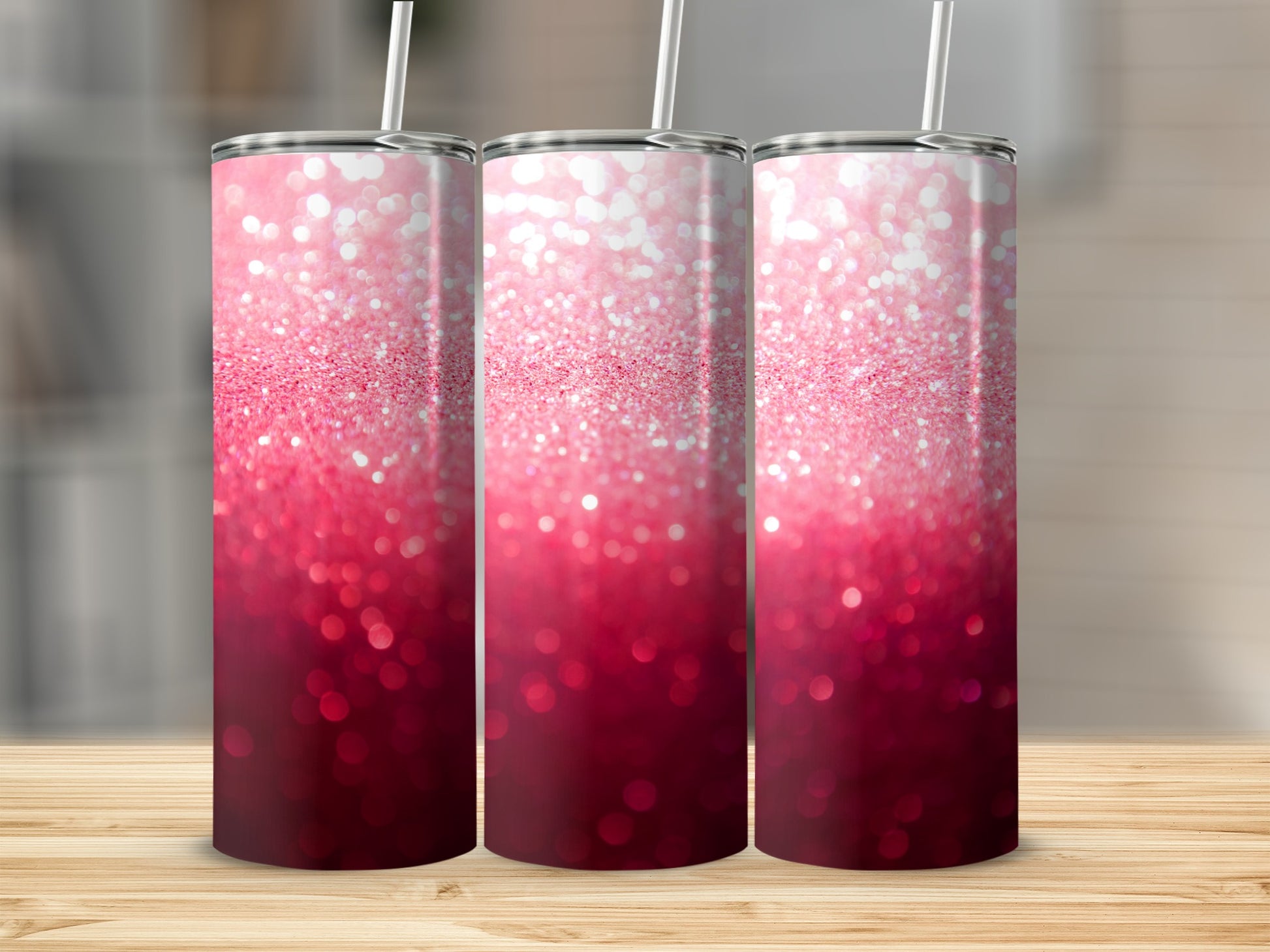 Three pink glitter tumblers with straws on a wooden surface.