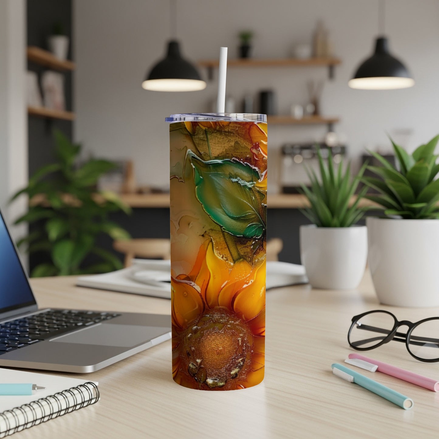 Sunflower tumbler with straw on a wooden desk with a laptop.