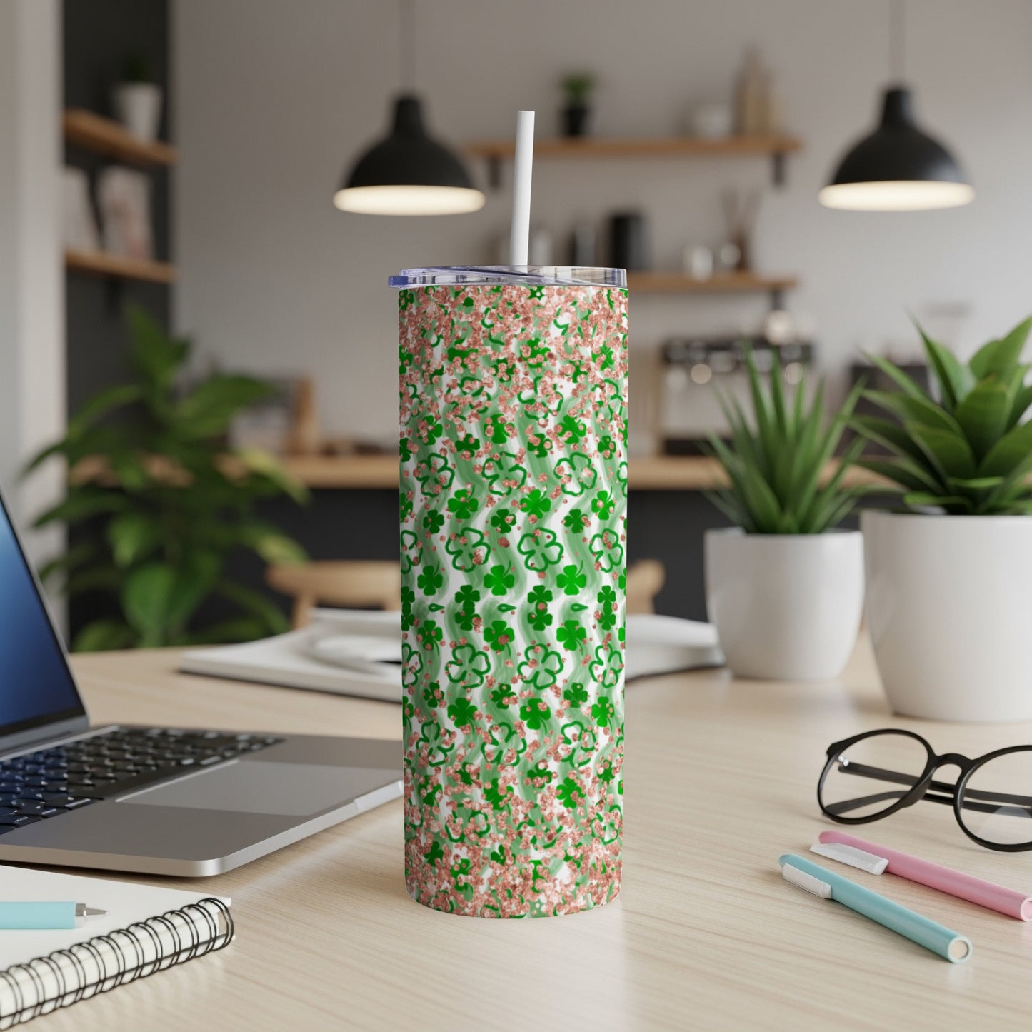 Green and pink glitter shamrock patterned tumbler with white straw on desk.