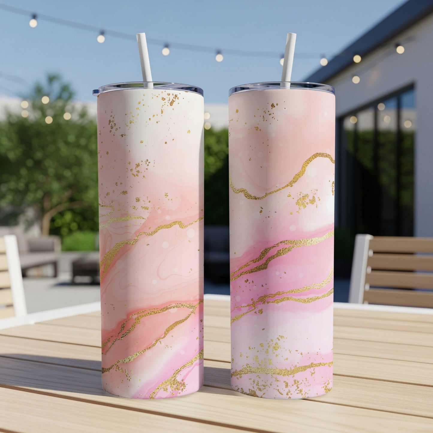 Two pink marbled tumblers with gold accents and straws on a wooden table.