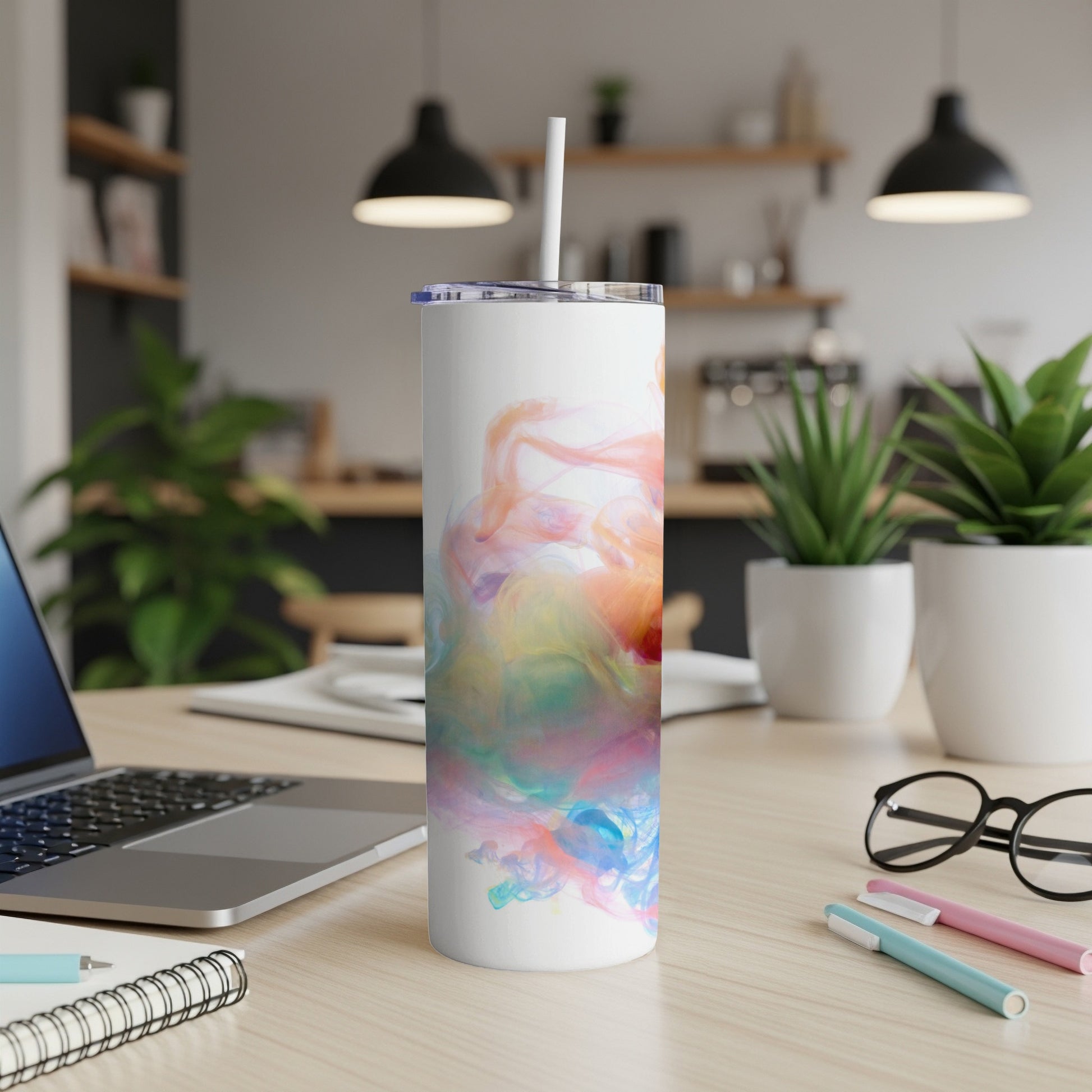 White tumbler with colorful abstract watercolor design, sitting on a desk.