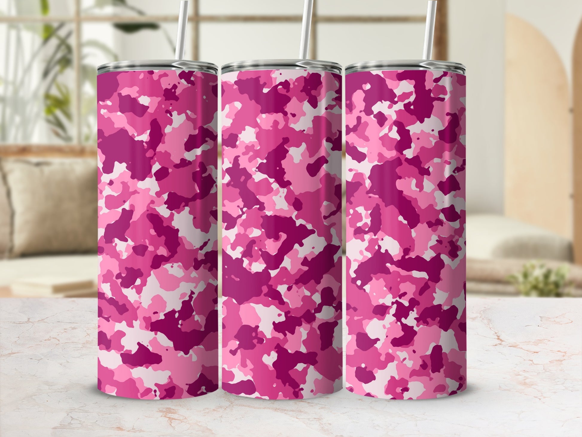Three tumblers with pink camouflage pattern and straws on a marble surface.