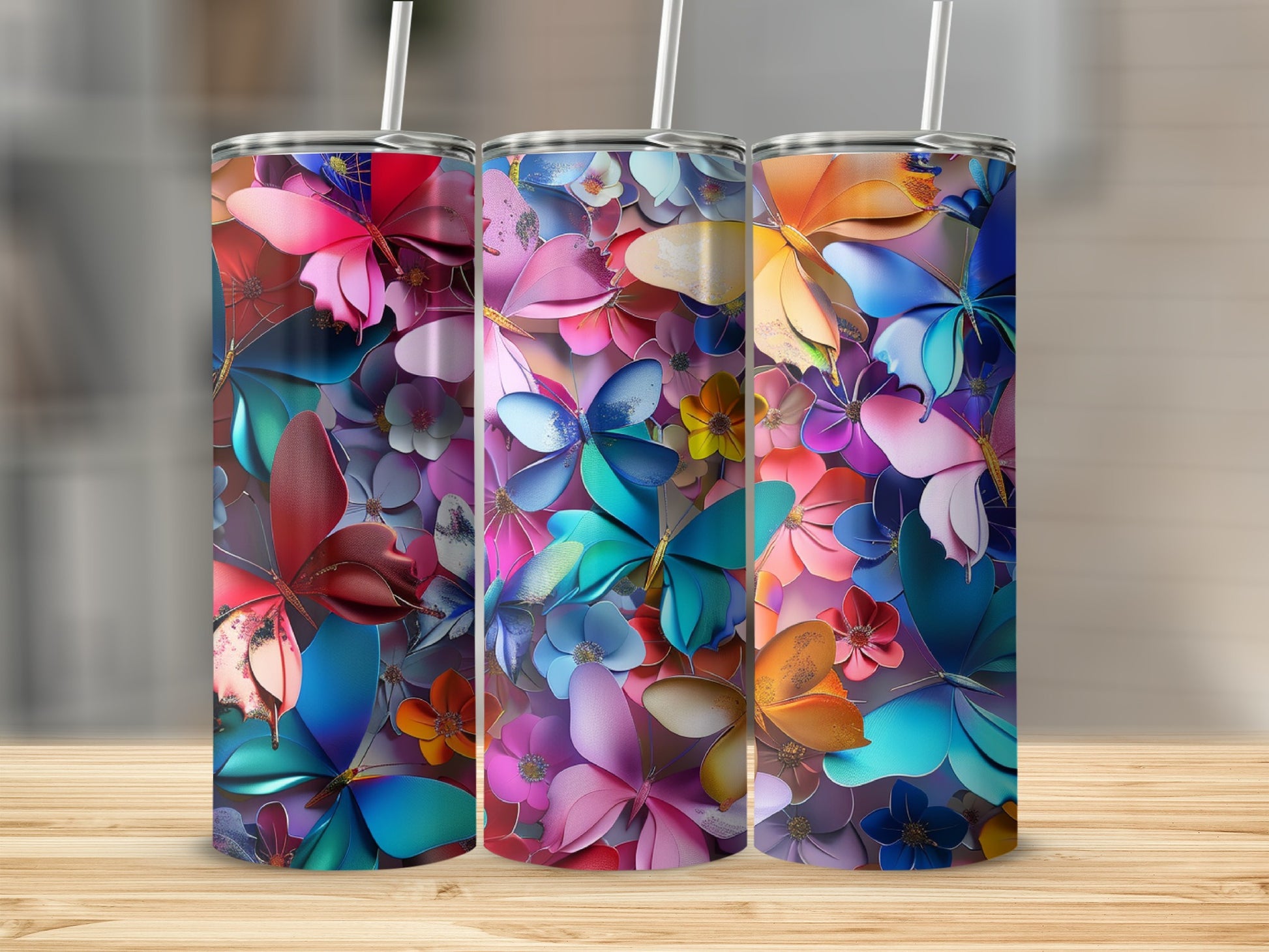 Three colorful butterfly and floral pattern tumblers with straws on a wooden surface.