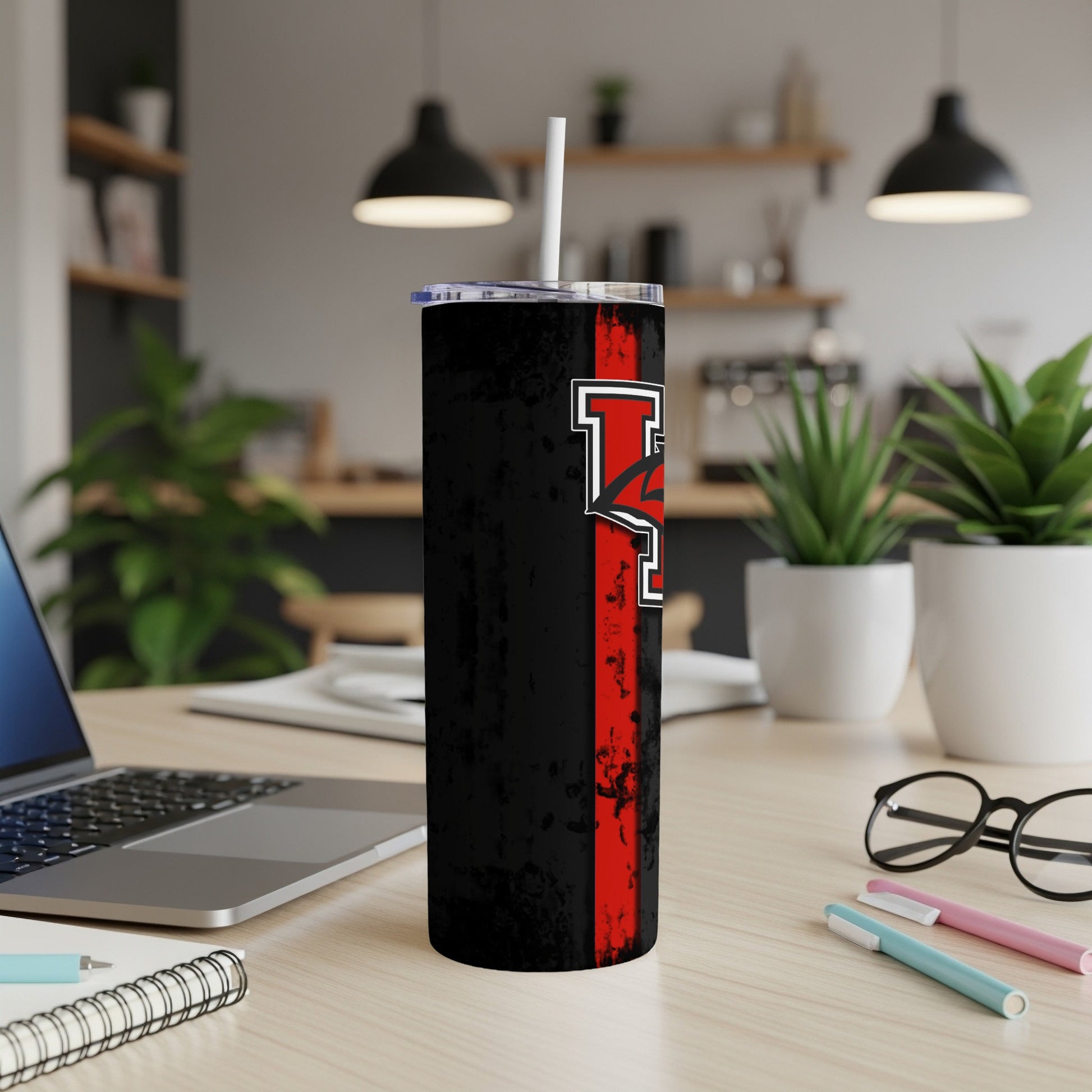 Black tumbler with red stripe and white-bordered red logo on desk.