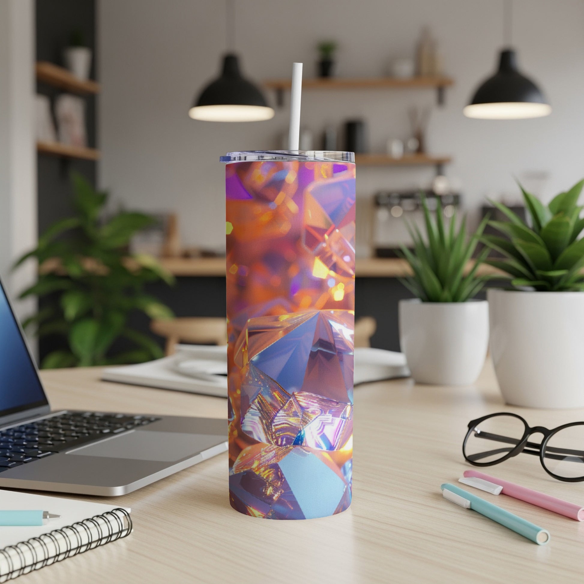 Colorful faceted tumbler with straw on a desk next to a laptop.