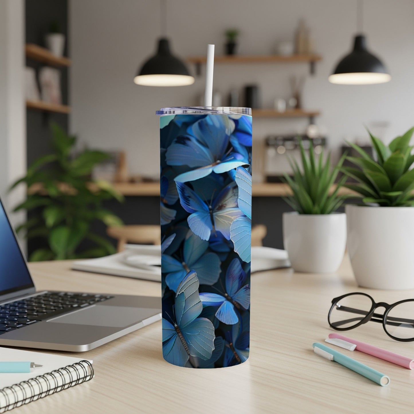 Blue butterfly patterned skinny tumbler with white straw on a desk.