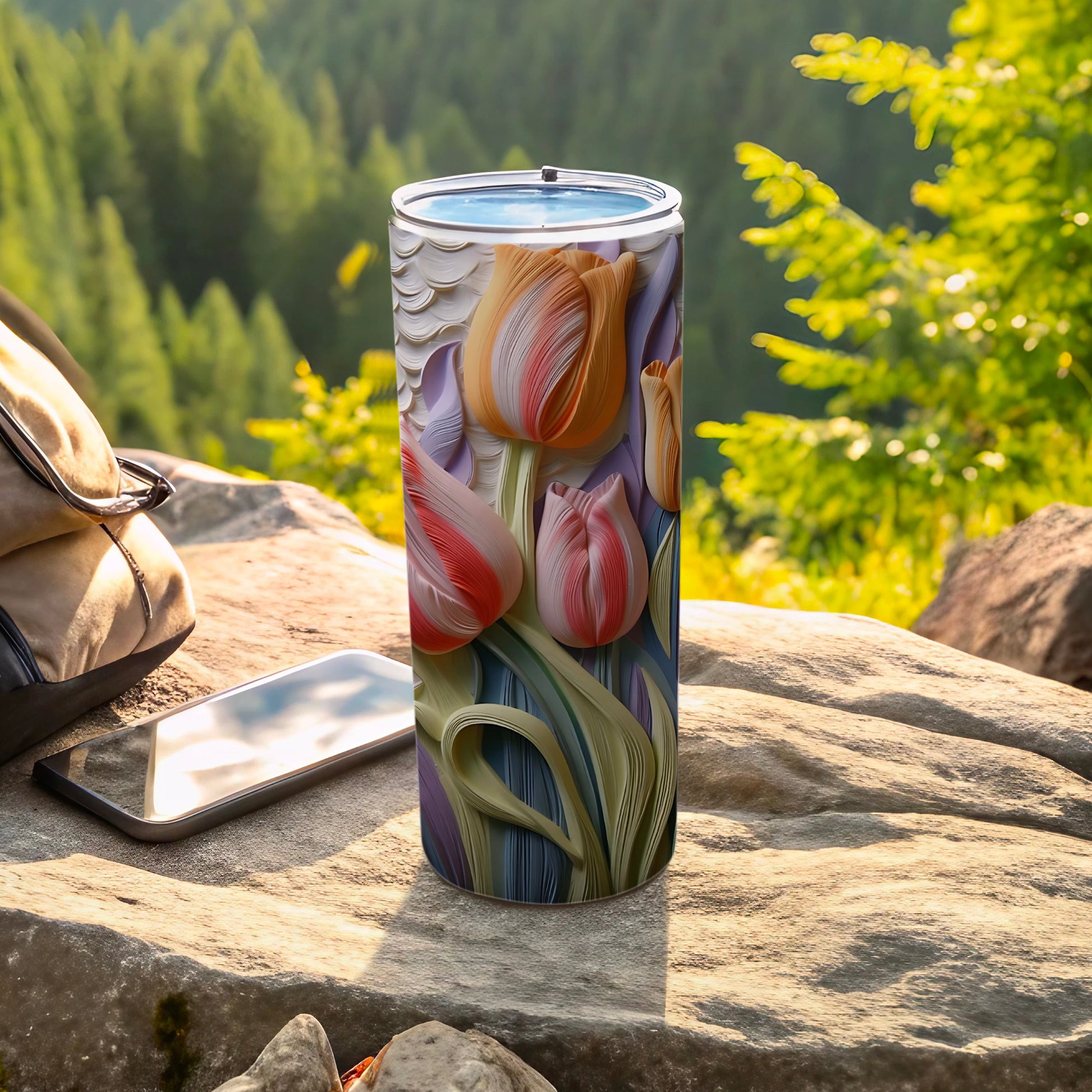 Tumbler with tulips design on rock with backpack and phone.