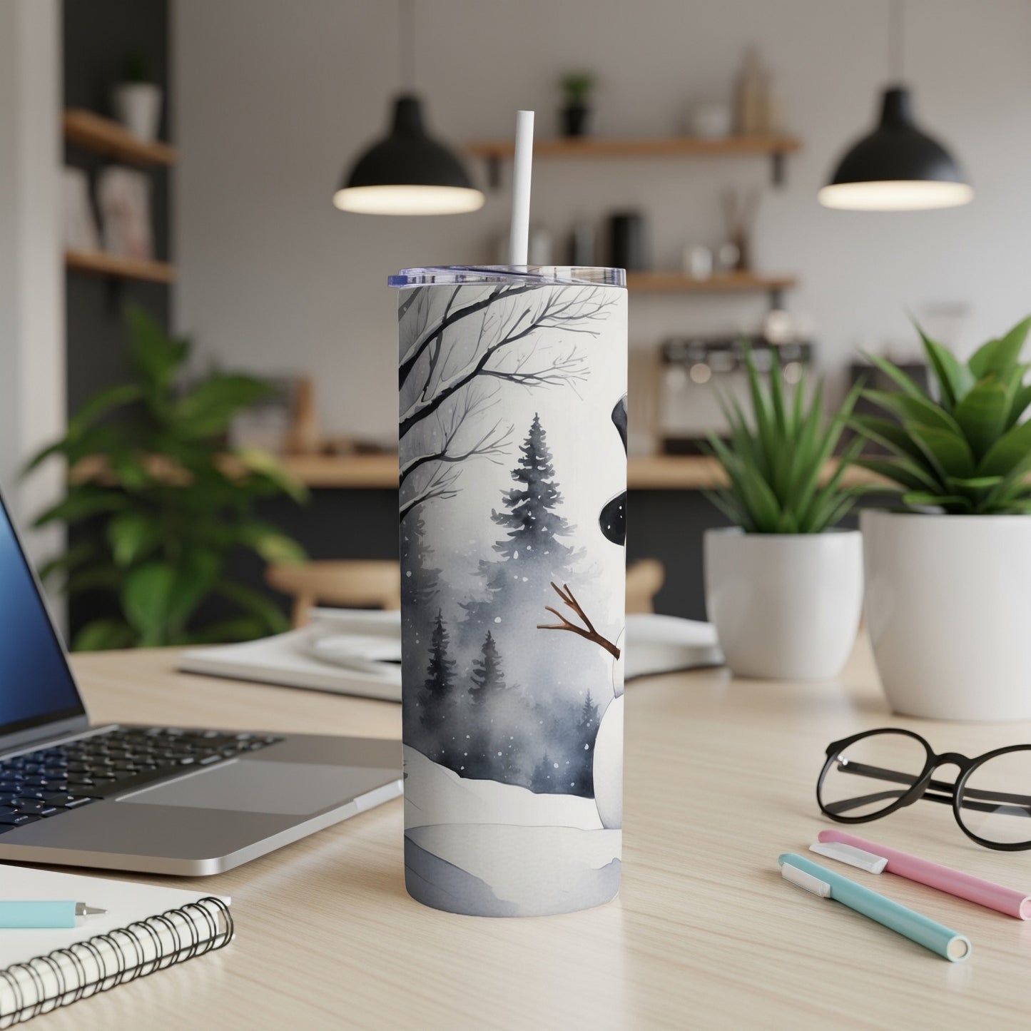 Snowman design on a white tumbler with a straw, set on a desk.
