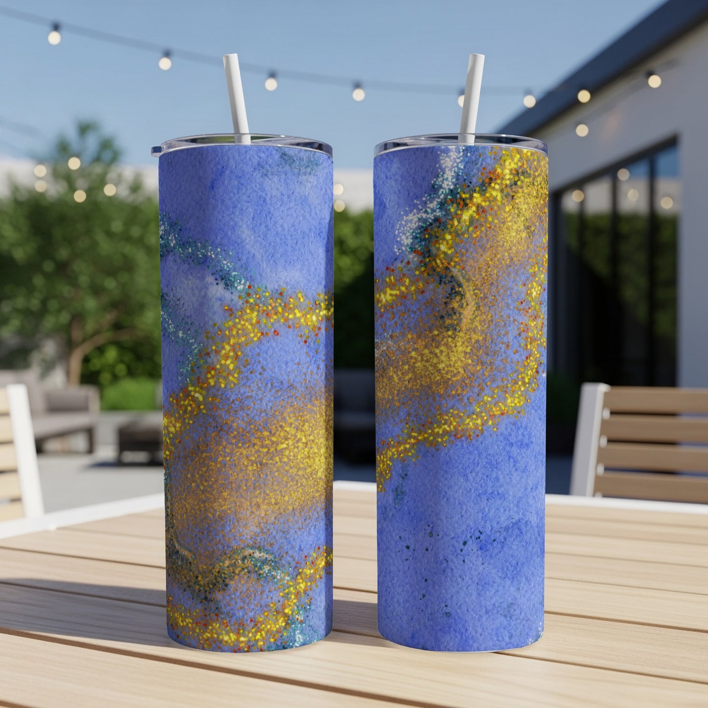 Two blue tumblers with gold glitter accents on a wooden table outdoors.