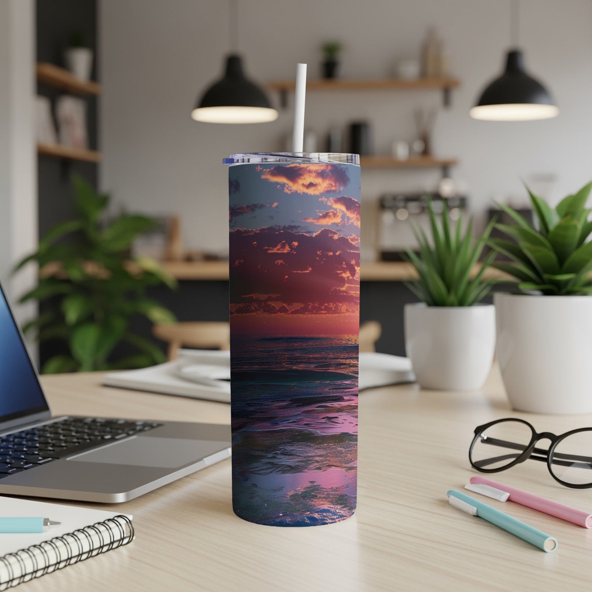 Sunset over ocean waves on a tumbler, placed on a desk with a laptop.