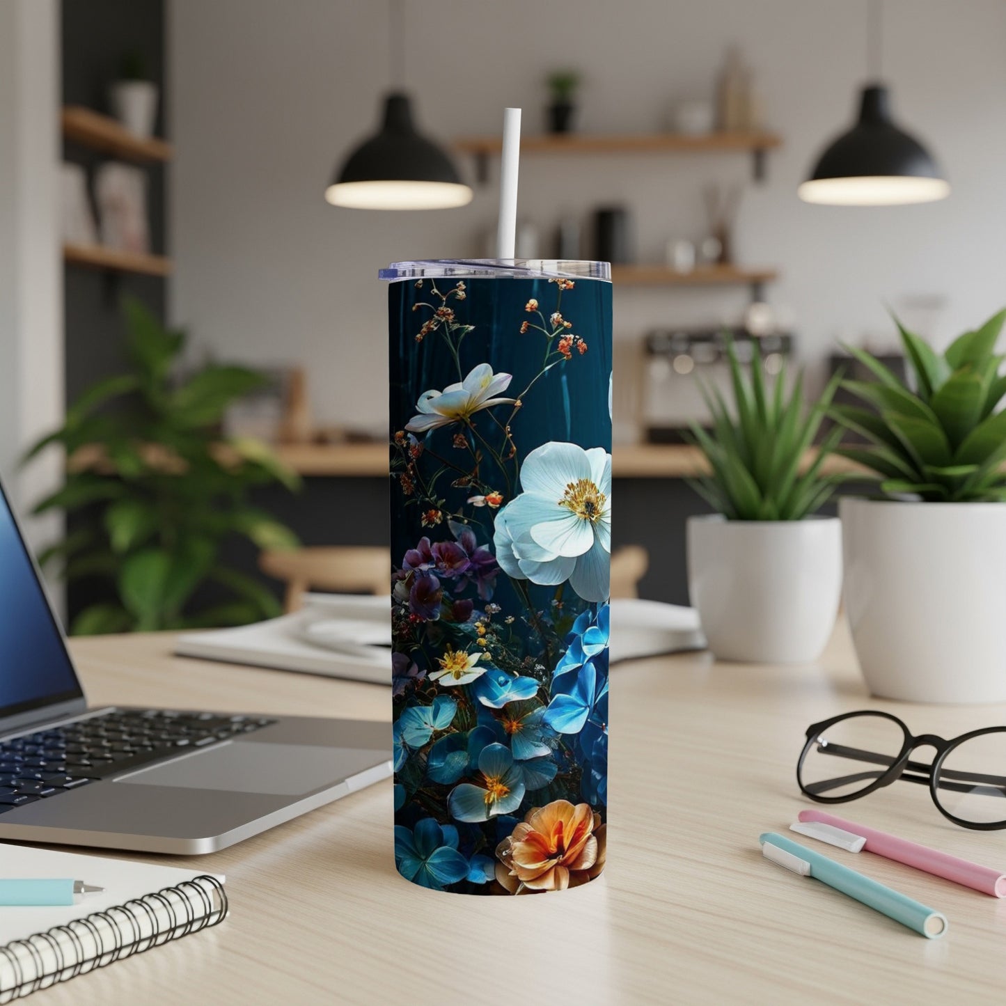 Dark tumbler with vibrant floral pattern on desk with laptop and pens.