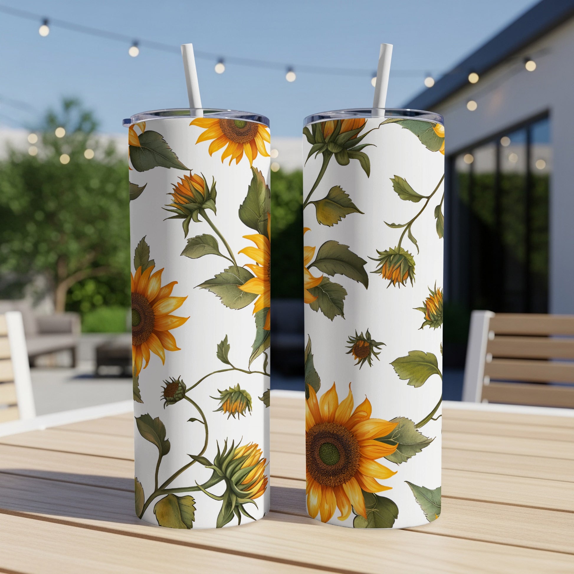 Two white tumblers with a sunflower pattern sit on a table outdoors.